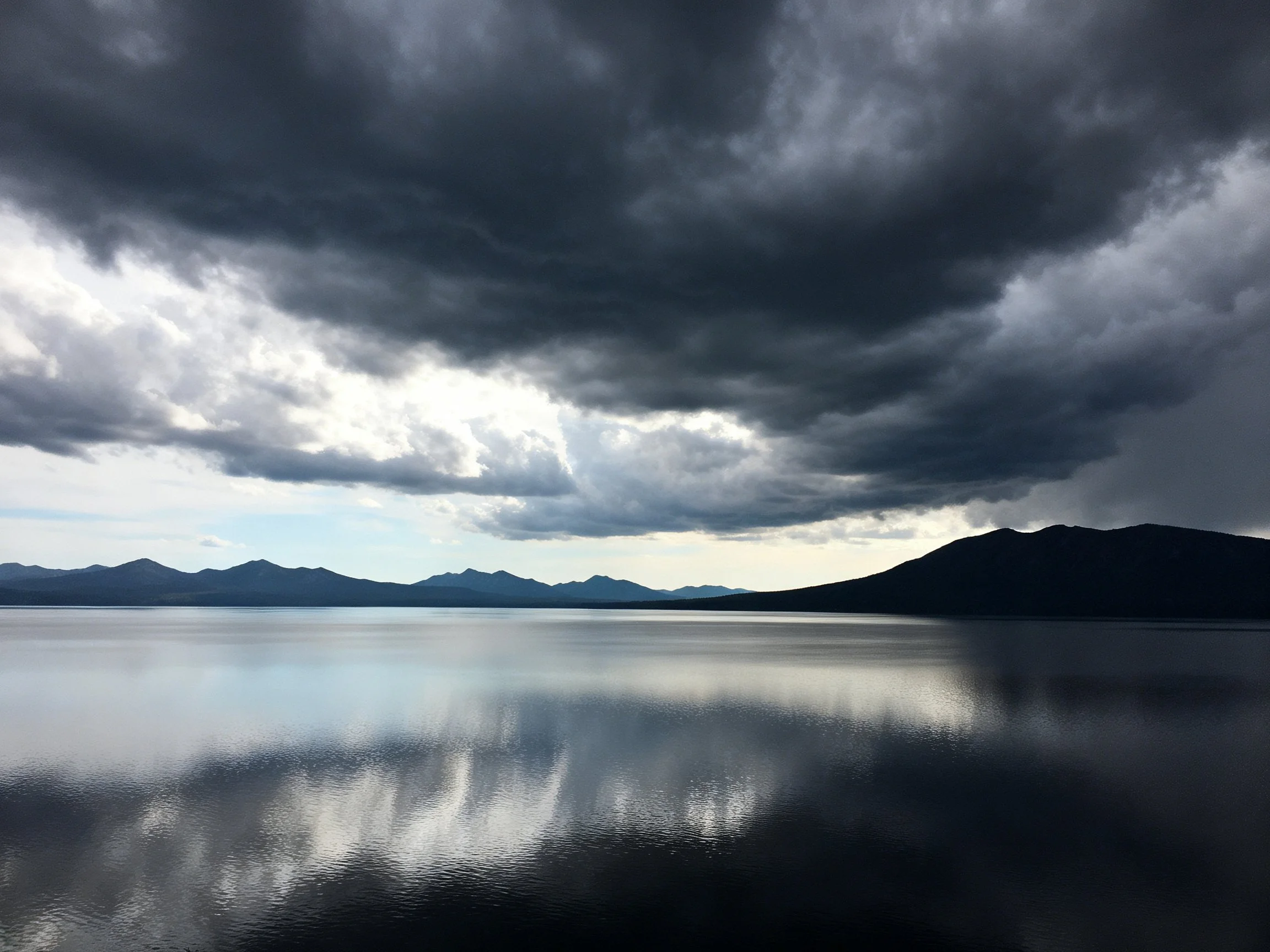 Dark storm clouds loom over a tranquil lake with mountain silhouettes.