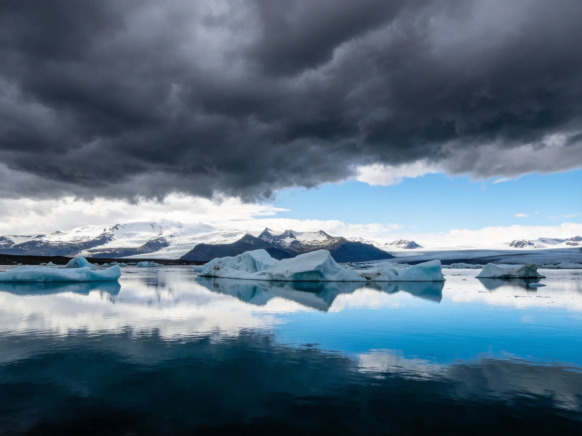 Dark storm clouds loom over an icy glacial lagoon with snowy mountains