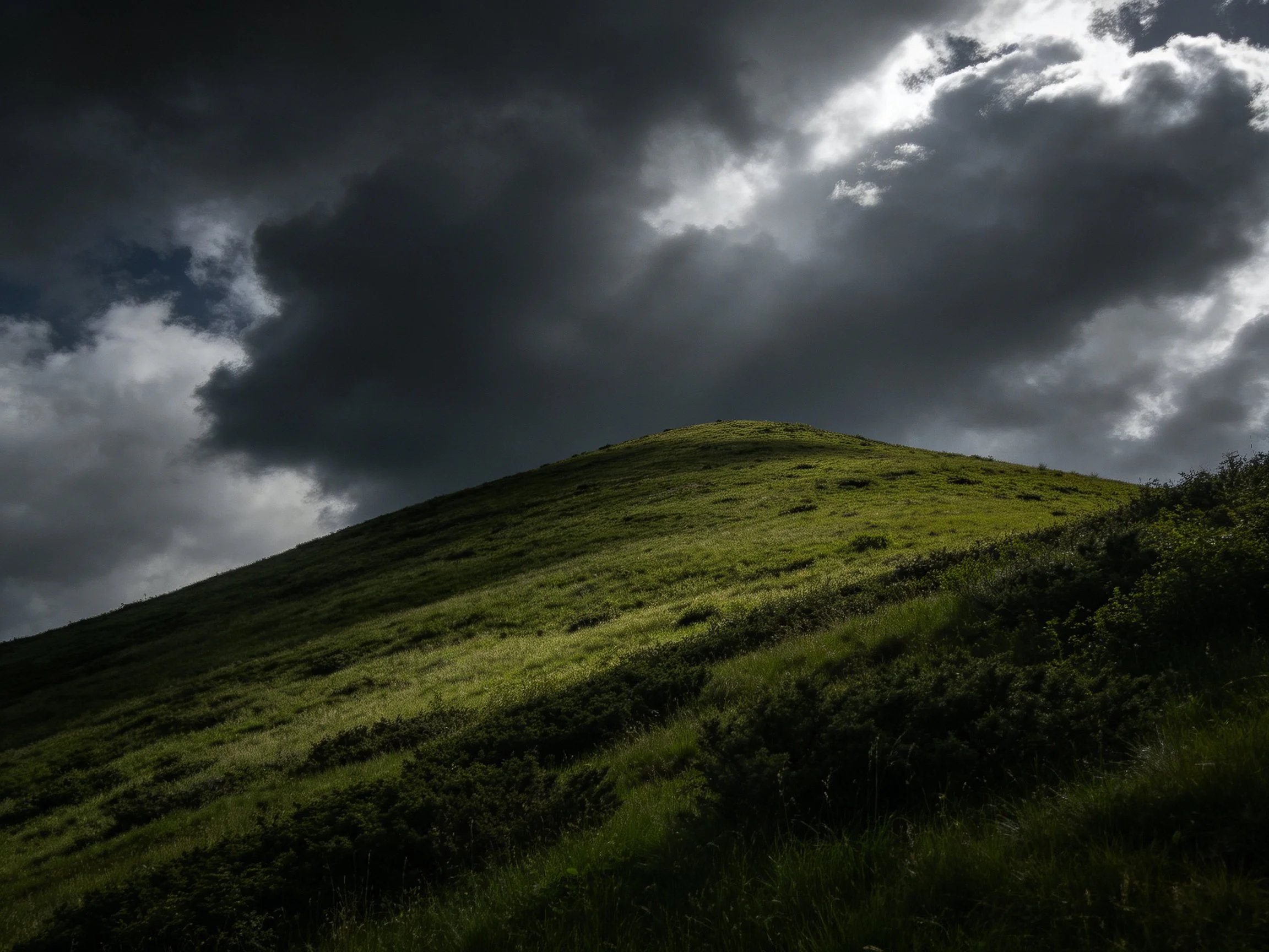 Dark storm clouds over a lush green hillside
