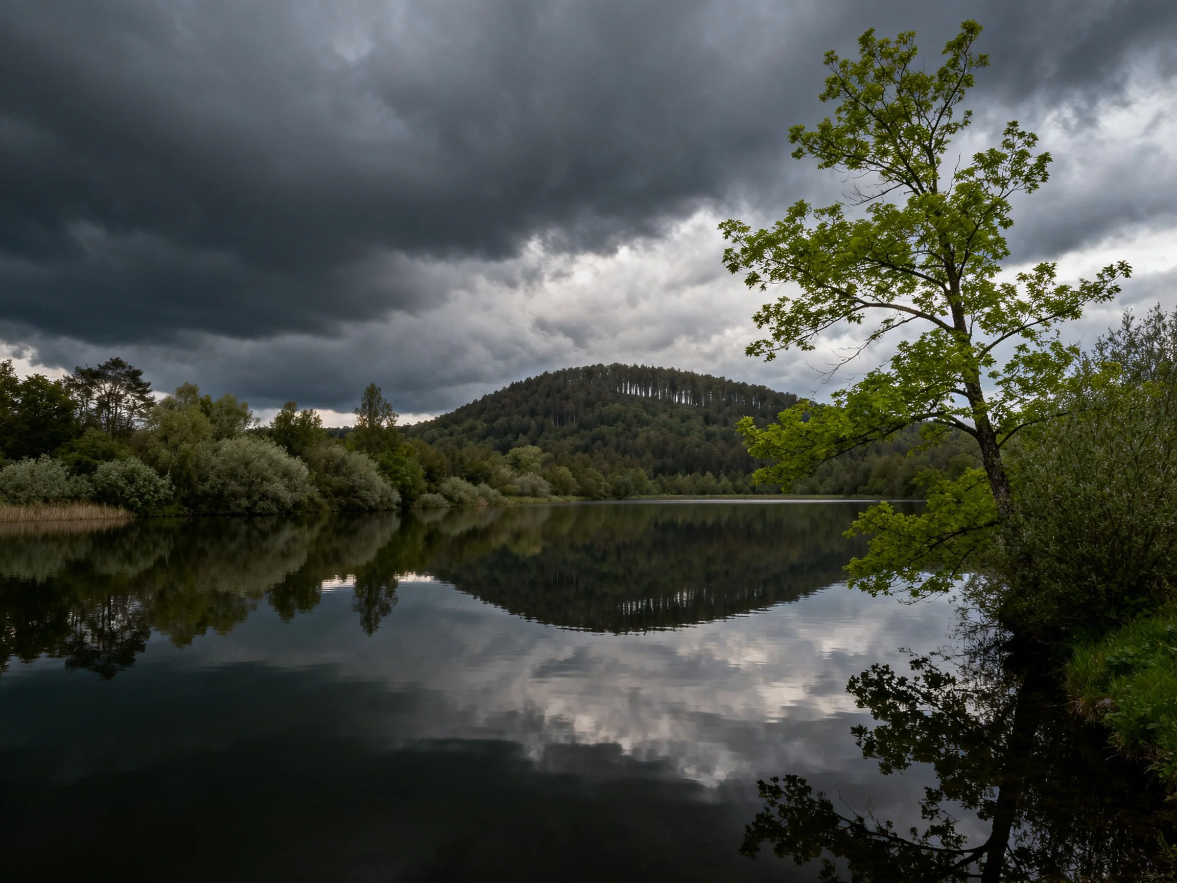 Dark storm clouds over a reflective lake with trees and hills