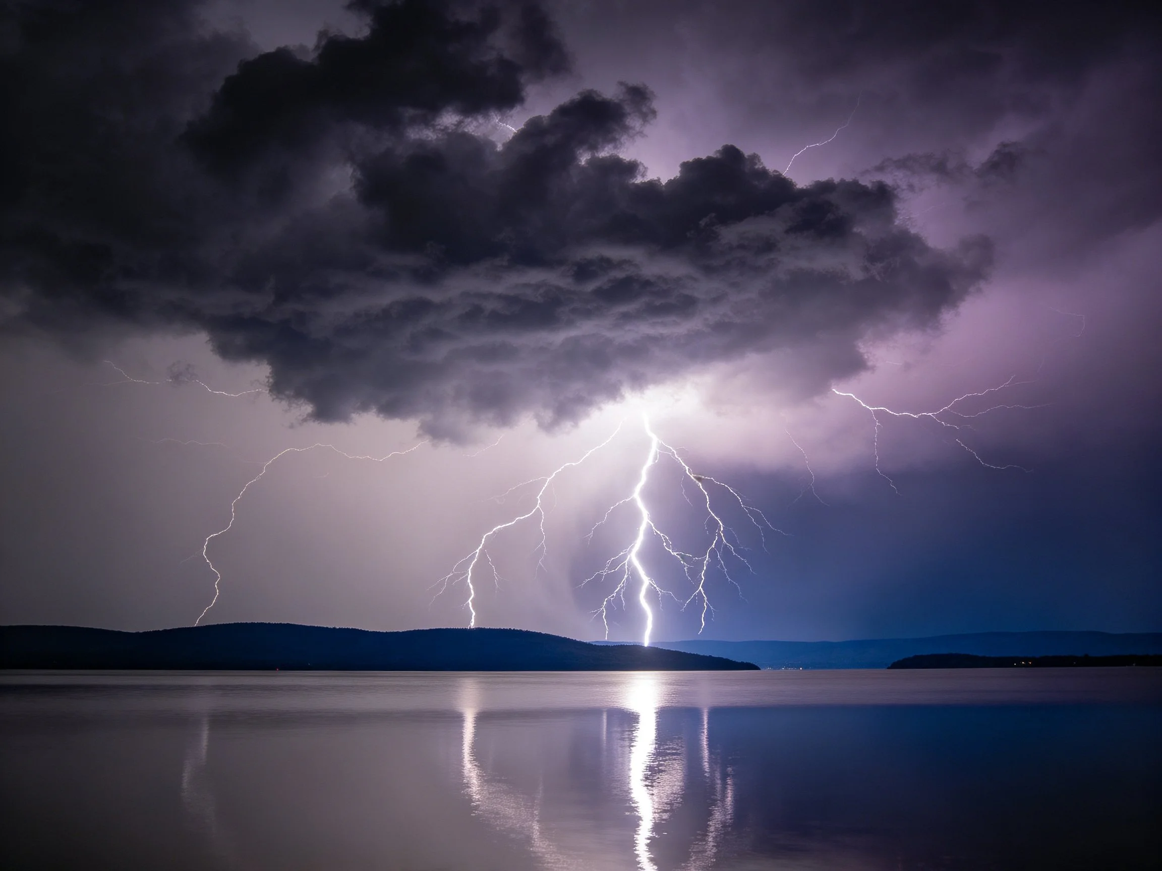 Dark storm clouds with bright lightning over calm water