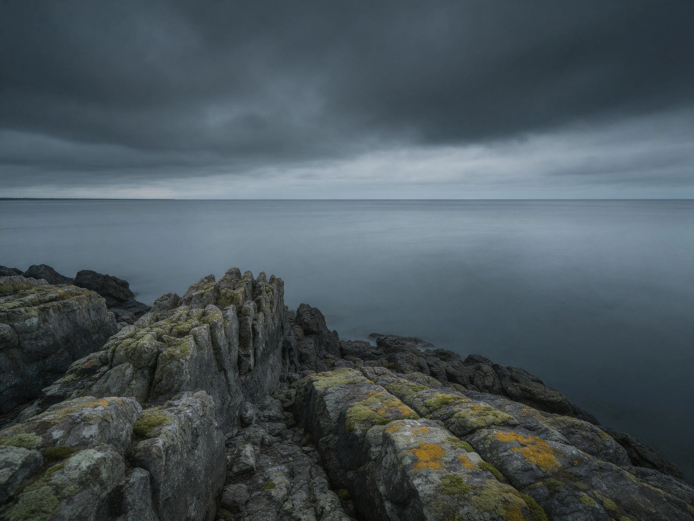 Dark stormy sky over rugged coastal rocks by calm water