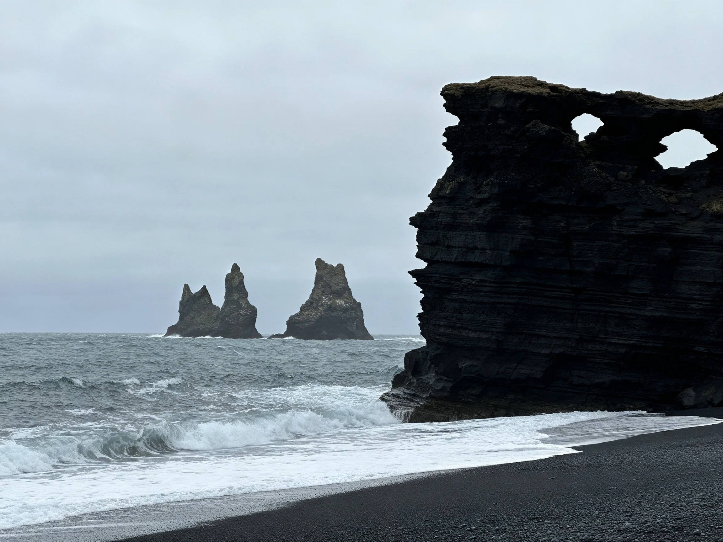 Dark volcanic cliffs by a black sandy beach with sea stacks