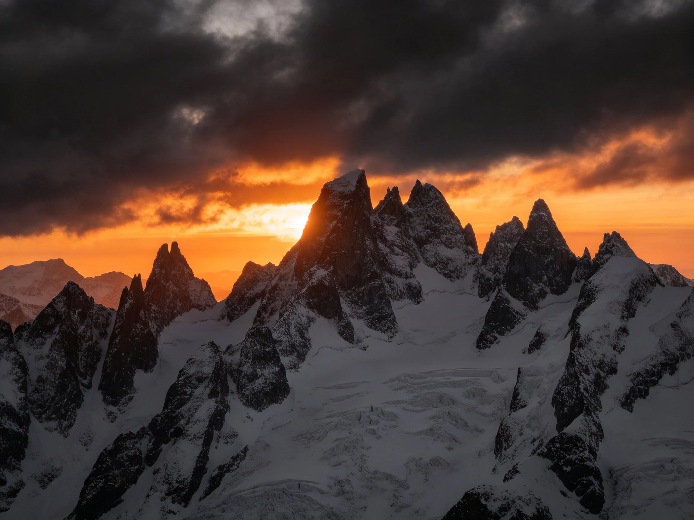Dramatic alpine landscape with jagged snow-capped peaks under stormy sunset skies