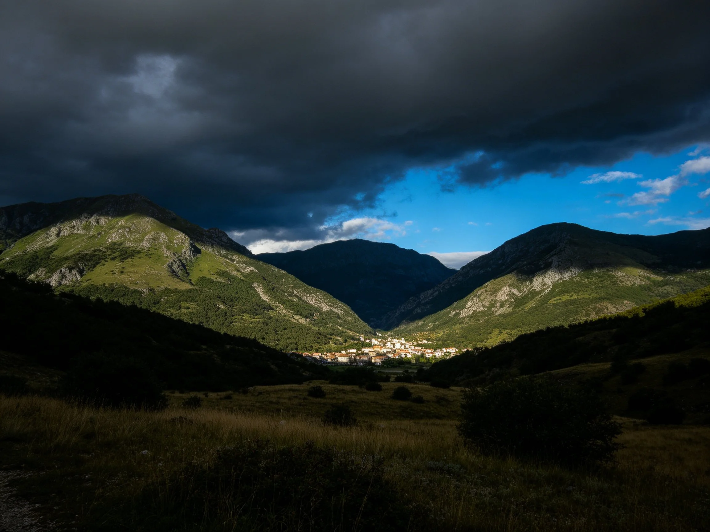 Dramatic mountain valley with stormy skies and a lit town