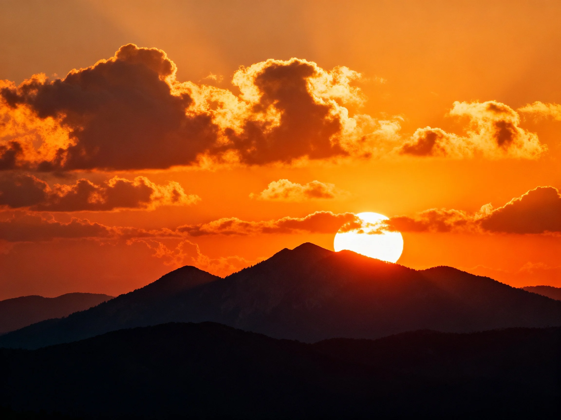Dramatic orange sunset behind mountain silhouettes with fluffy clouds