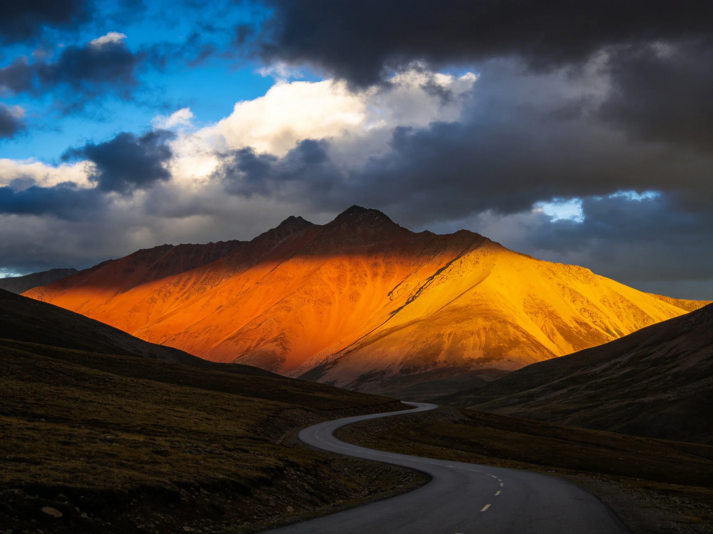 Dramatic sunset illuminates golden mountain with winding road