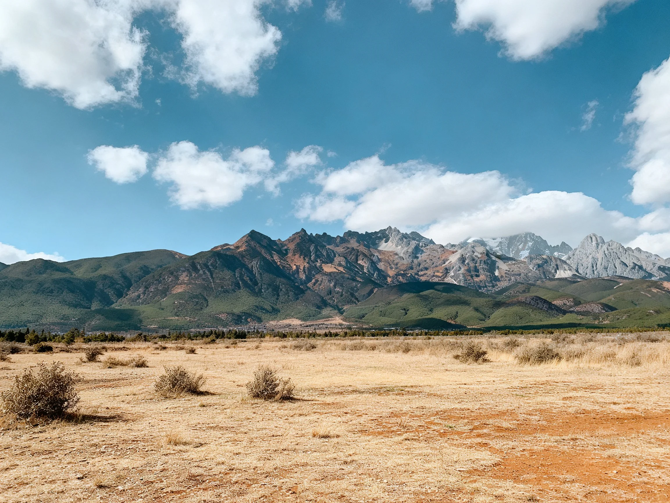 Expansive dry plain meets rugged mountain peaks beneath a bright blue sky.