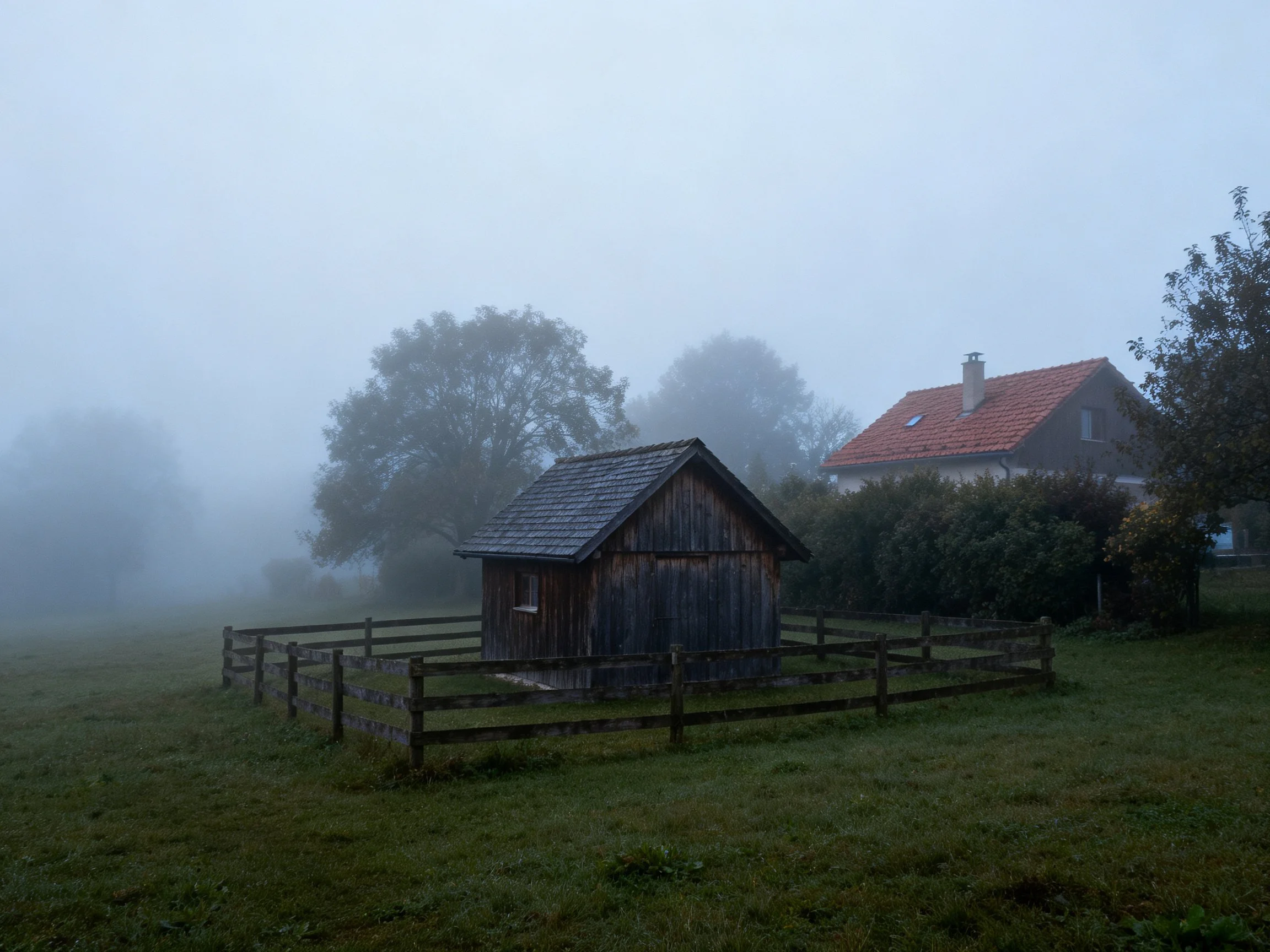 Foggy Rural Scene with Weathered Wood Shed and Red-Roofed House