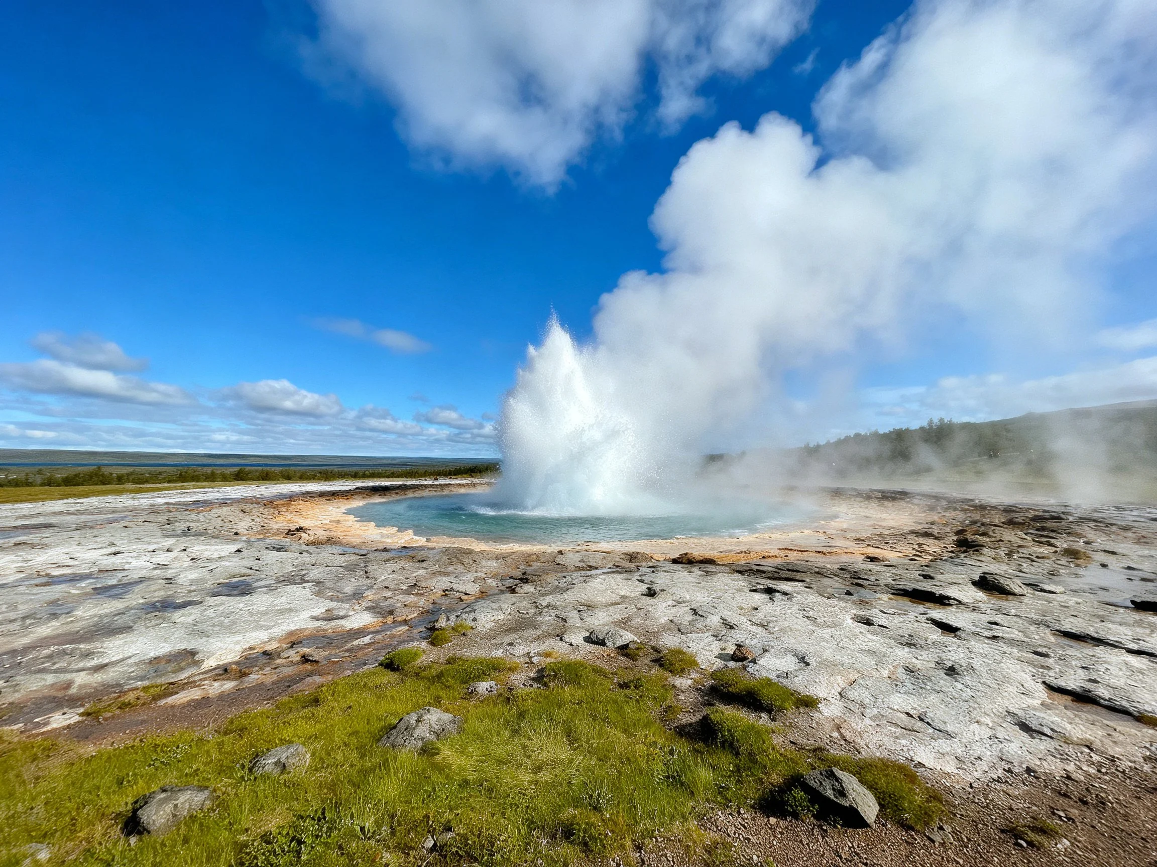 Geothermal geyser erupting with white steam and mineral deposits