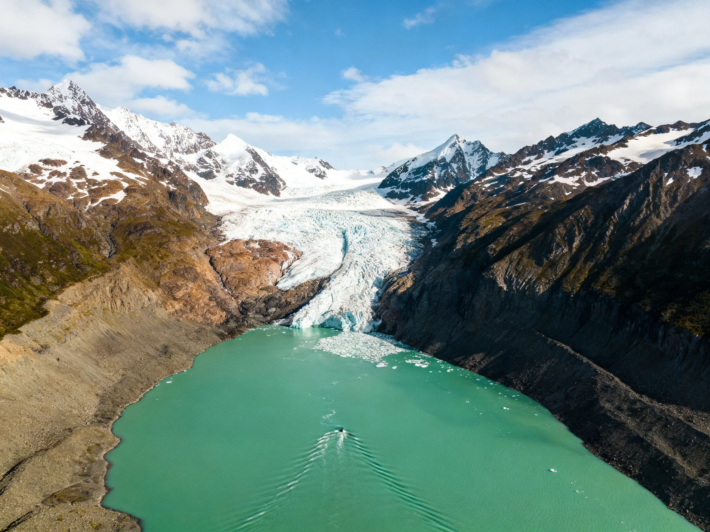 Glacial - fed turquoise lake between snow - capped mountains with a boat