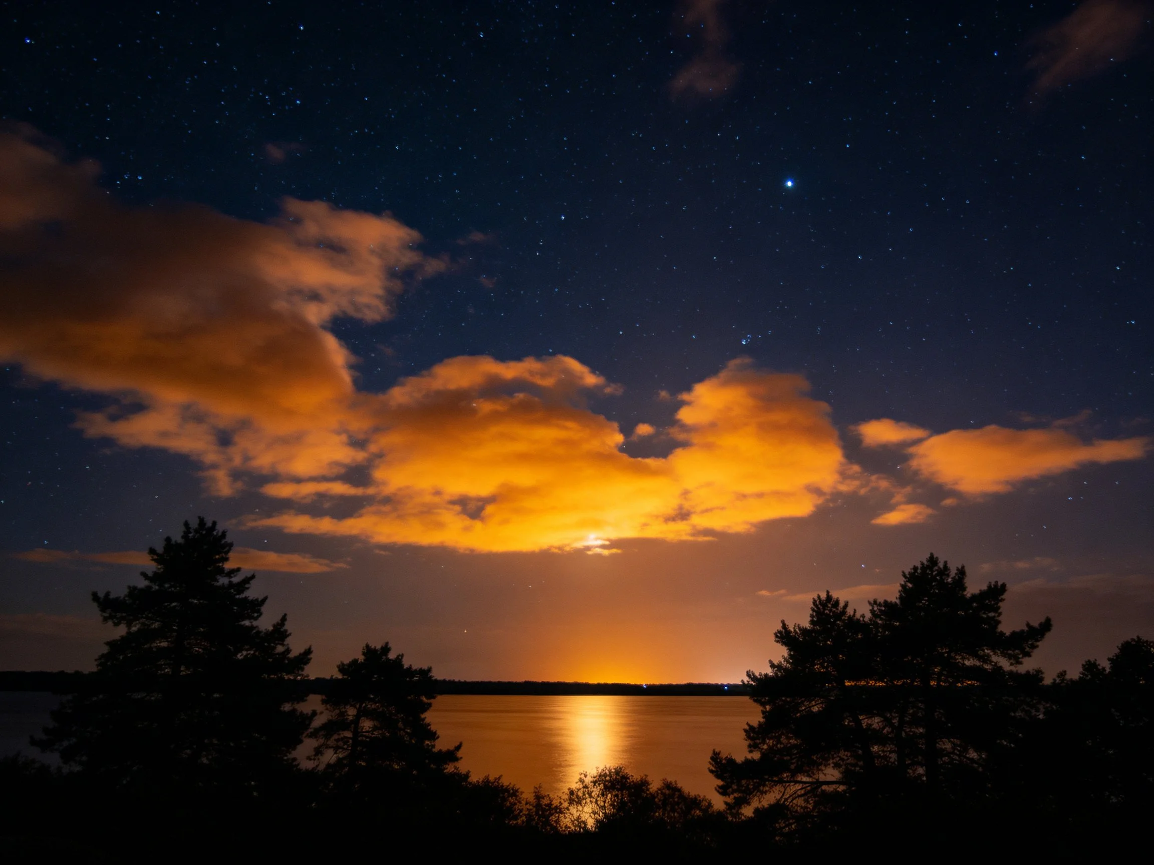 Glowing Orange Clouds Over Calm Water Under Starry Night Sky