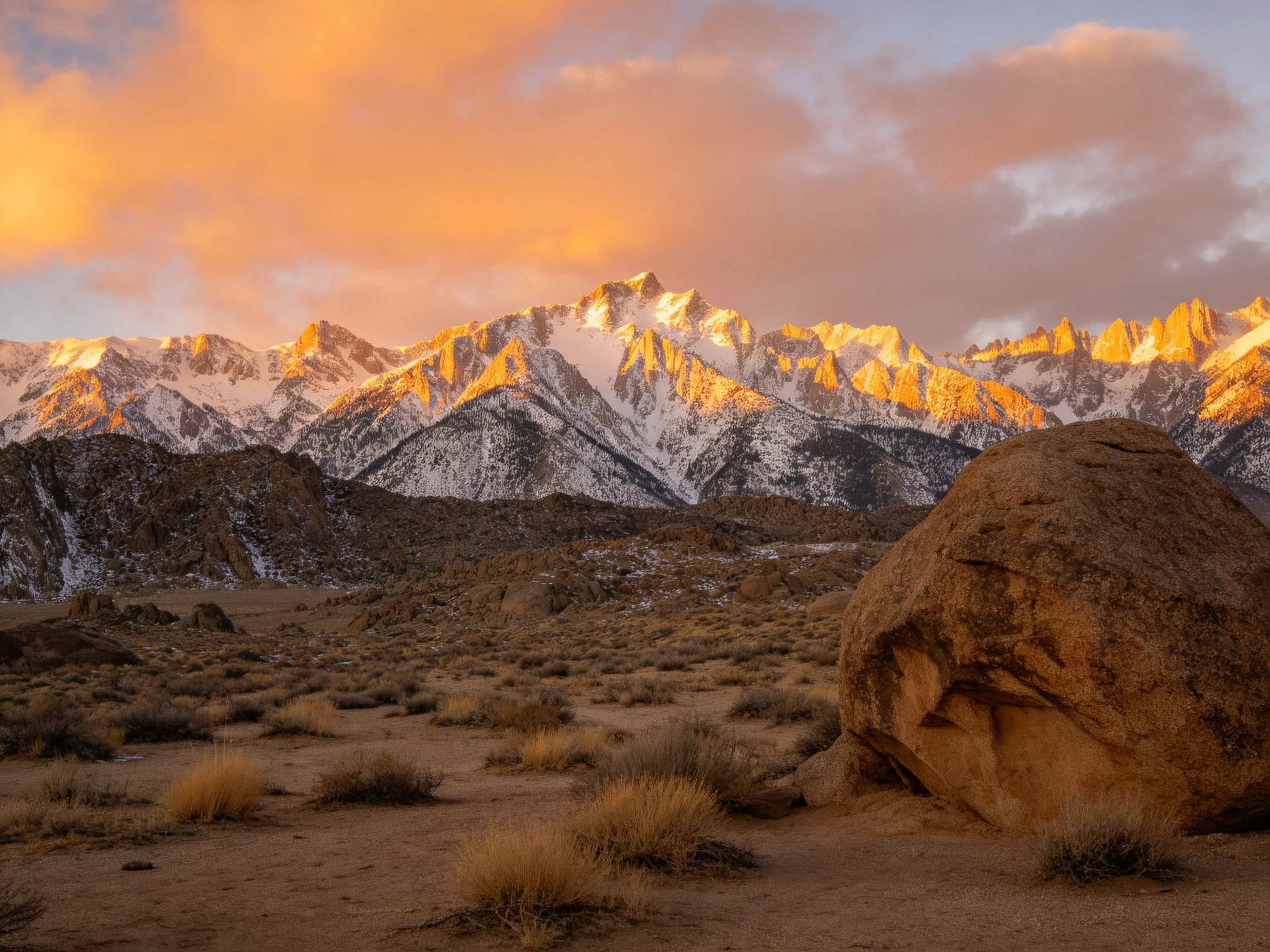 Golden Sunset Illuminates Snow-Capped Mountain Peaks Near Desert Boulders