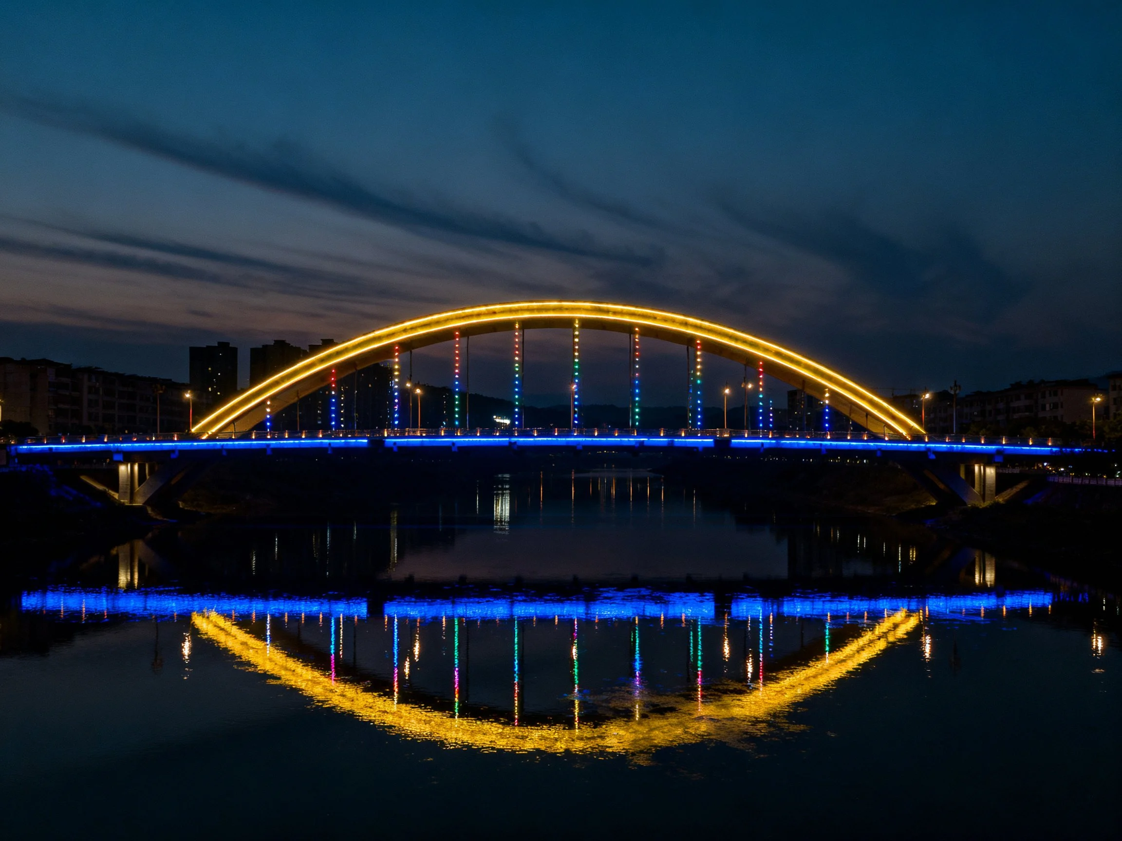 Golden and blue lit arch bridge reflecting on water