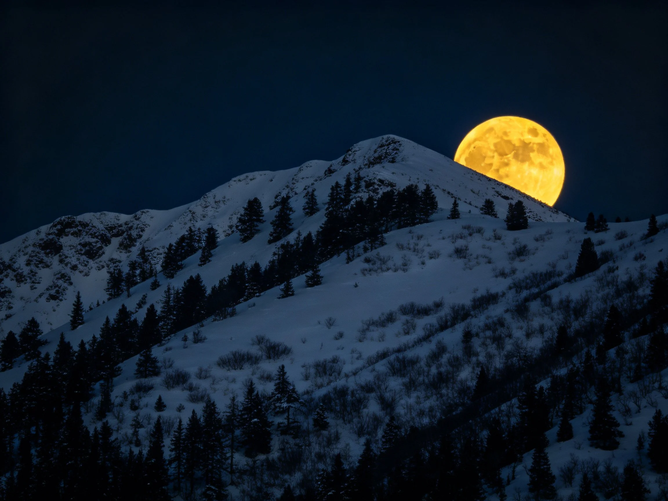 Golden full moon rises behind snow-covered mountain peaks