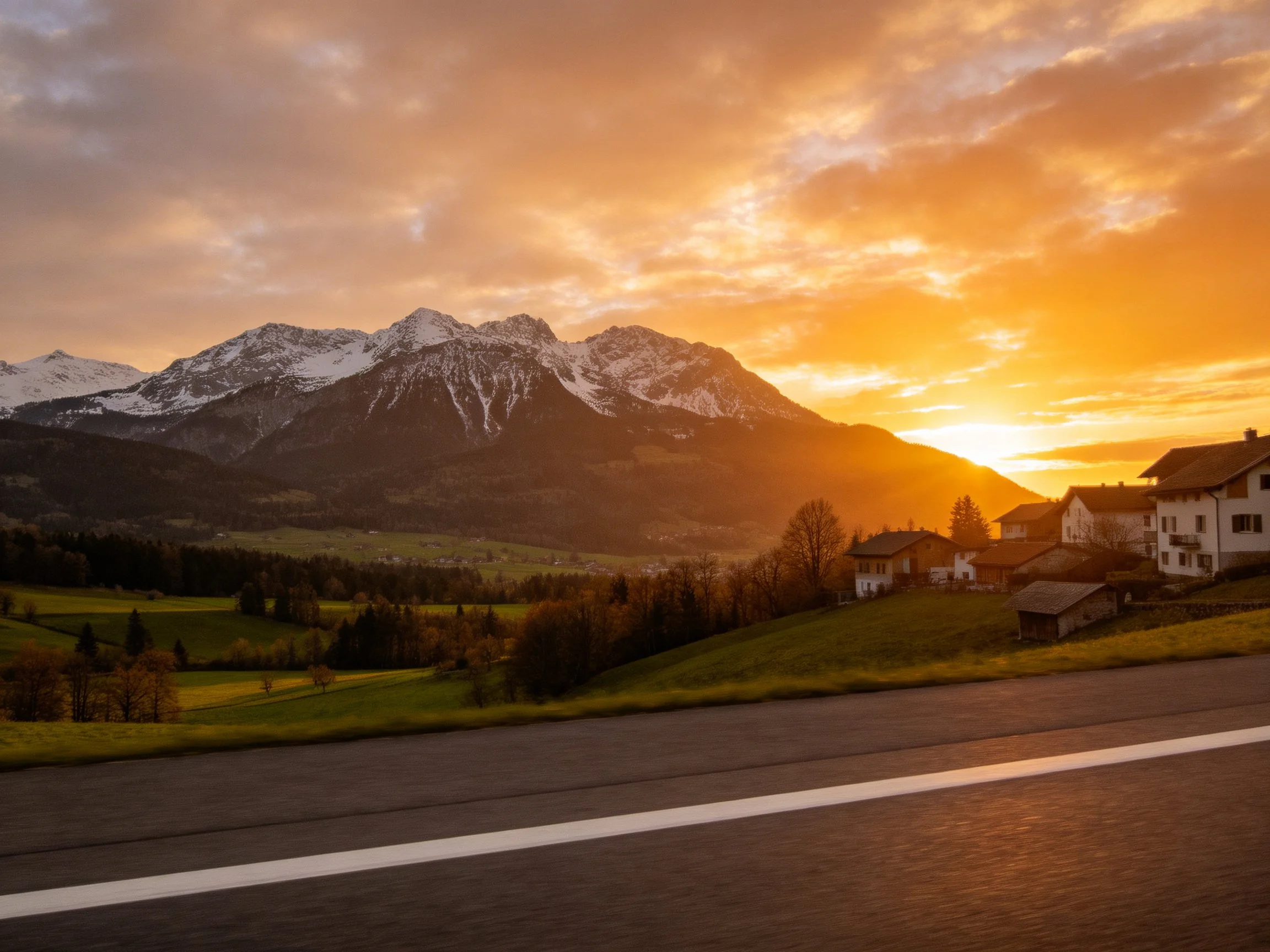 Golden-hour sunset over snow-capped mountains and rural village