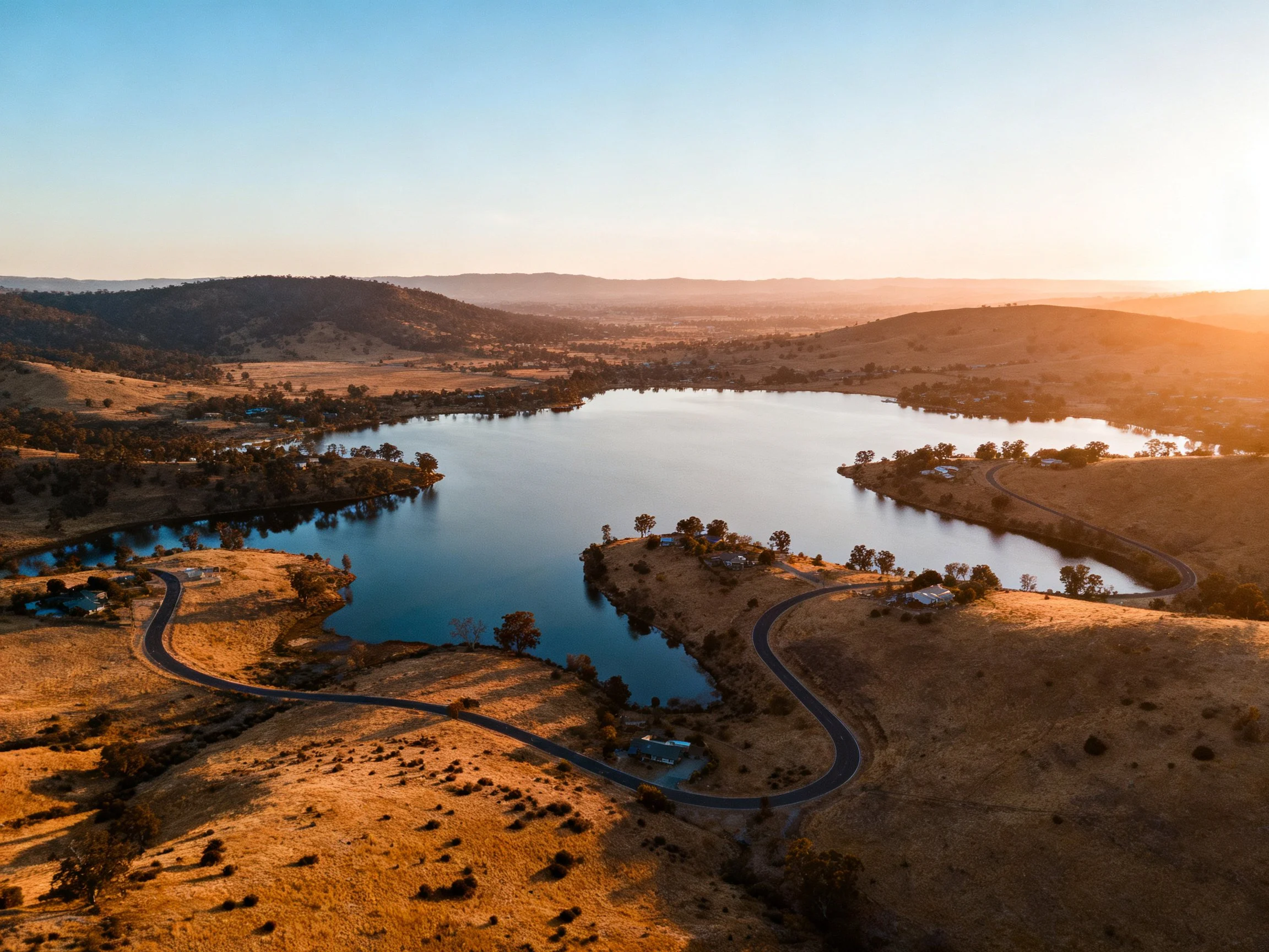 Golden-hued landscape with a large lake, rolling hills, and winding roads