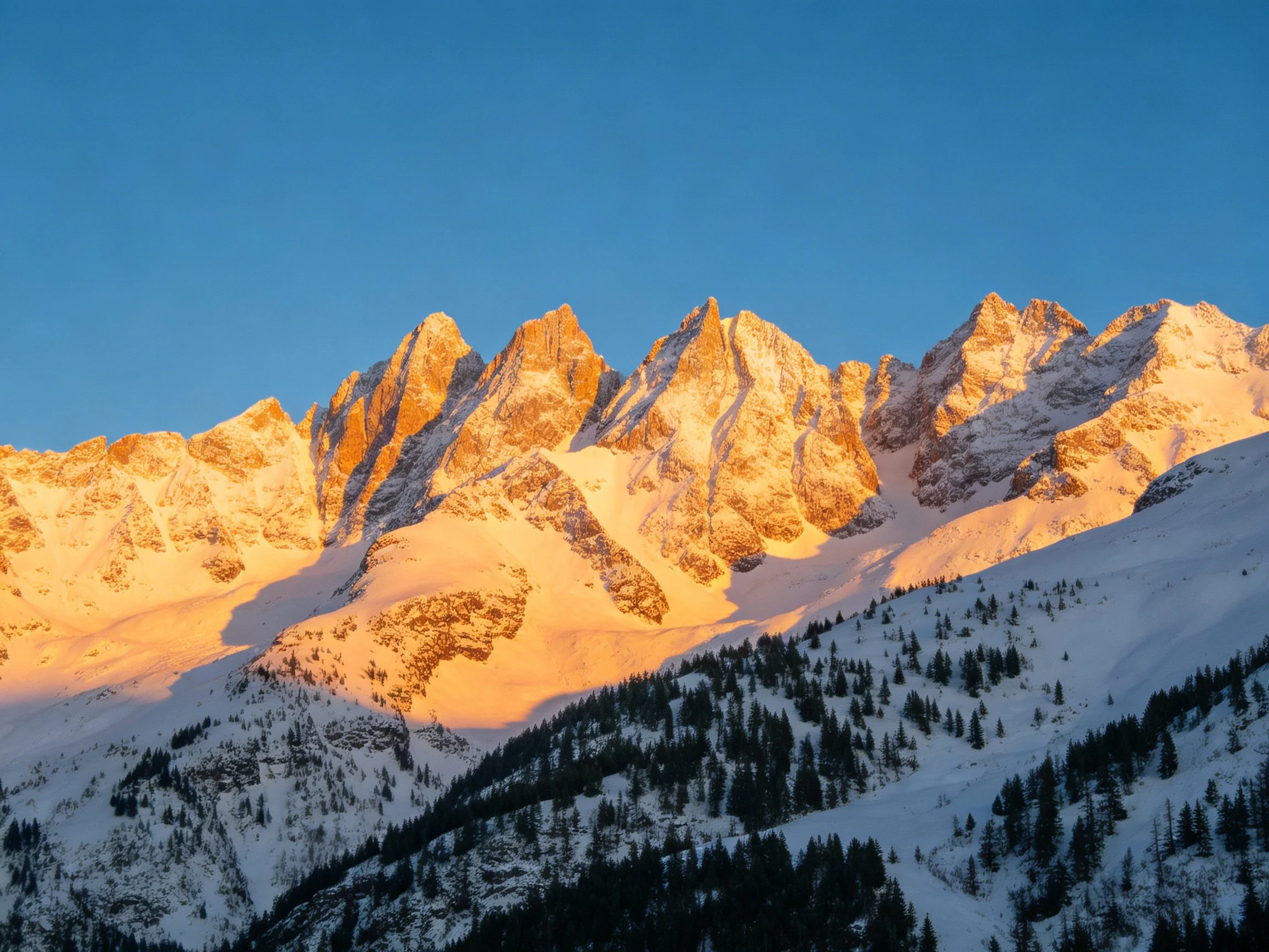 Golden-hued snow-capped mountain peaks against clear blue sky