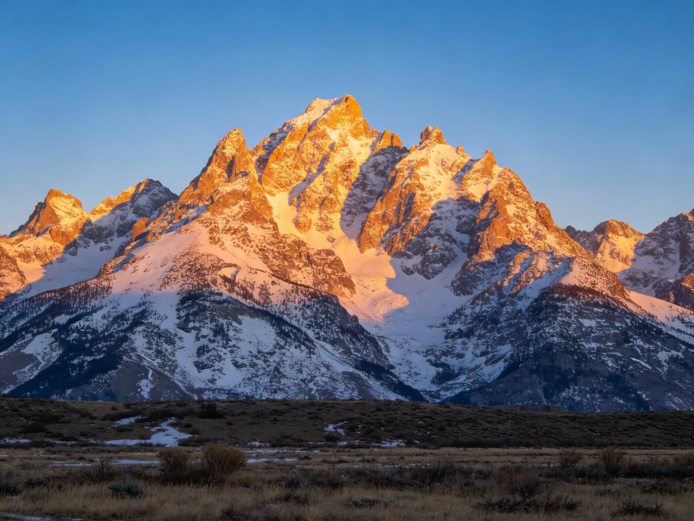 Golden-hued snow-capped mountain range against clear blue sky