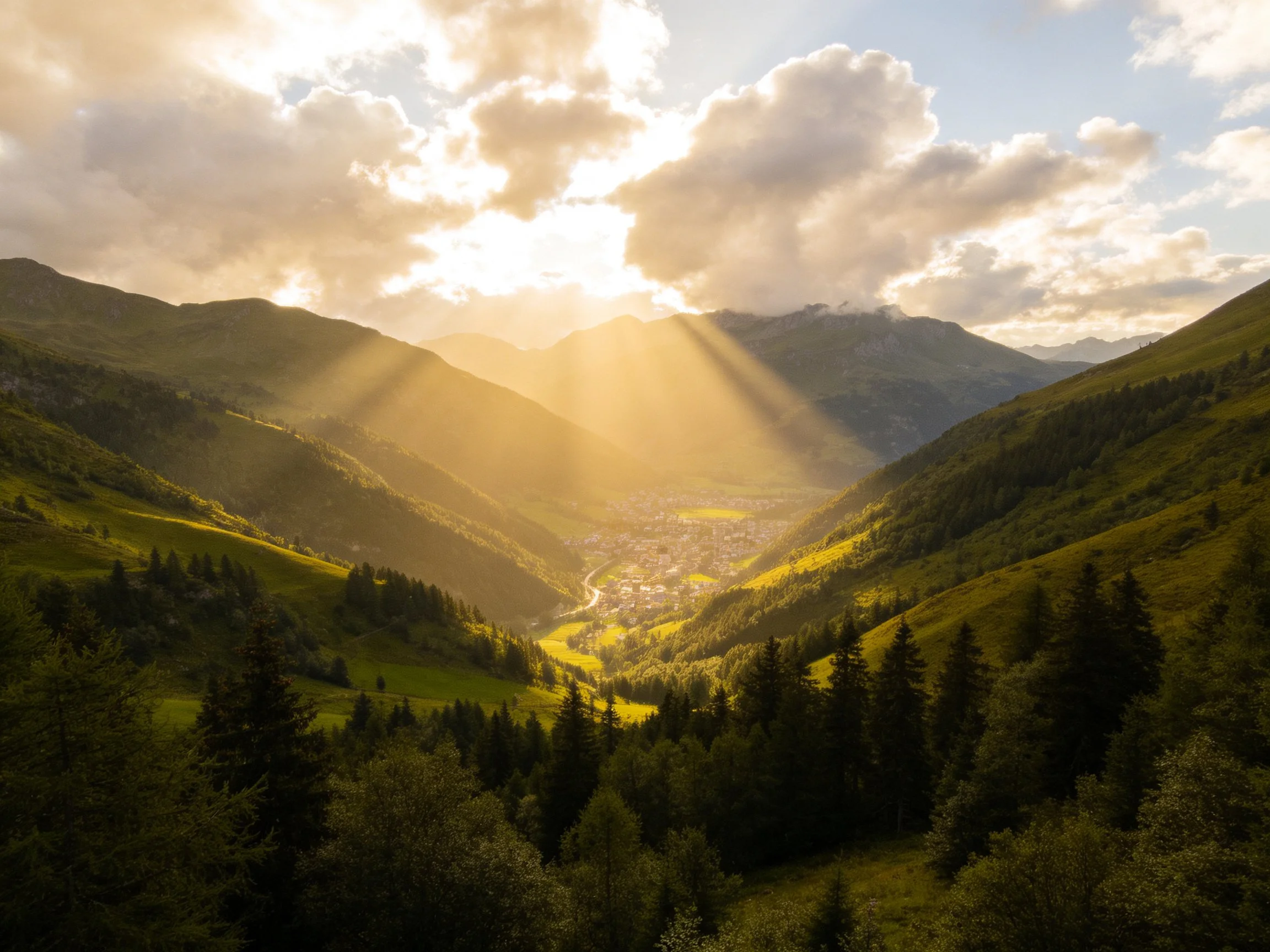 Golden sunbeams illuminate a lush mountain valley with a central town