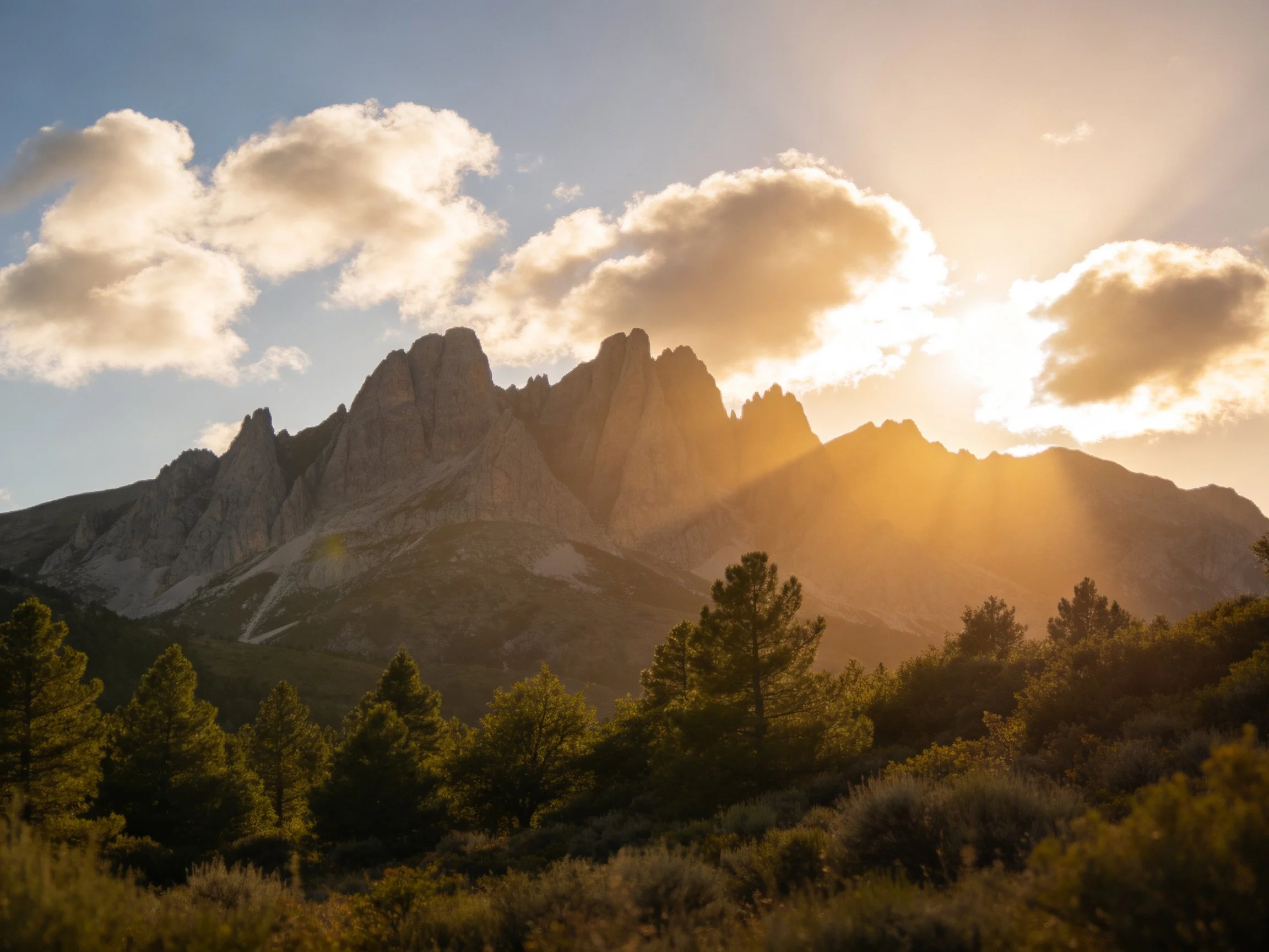 Golden sunlight illuminates dramatic rocky peaks with forested foreground