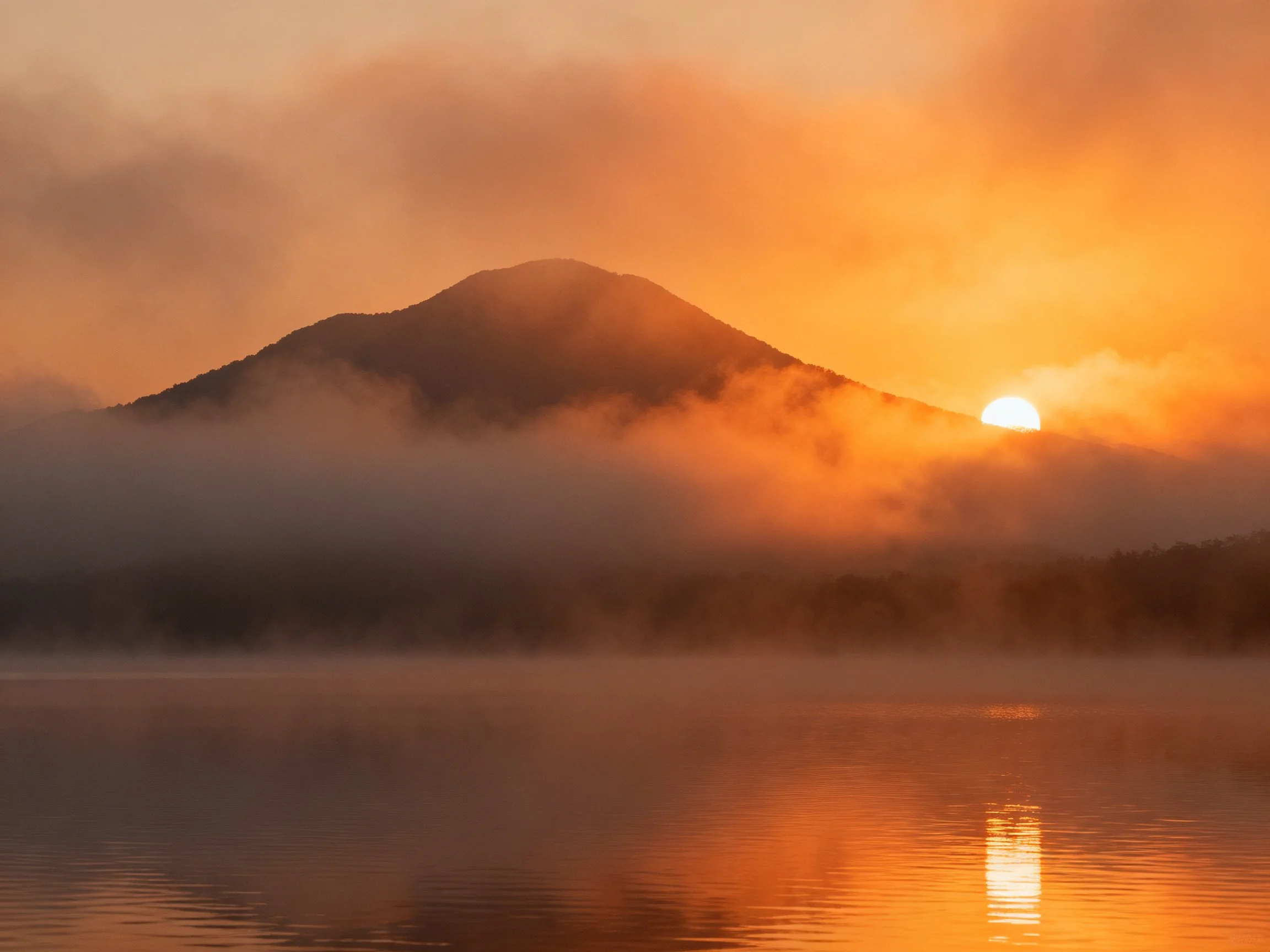Golden sunrise illuminates misty mountain with reflective water
