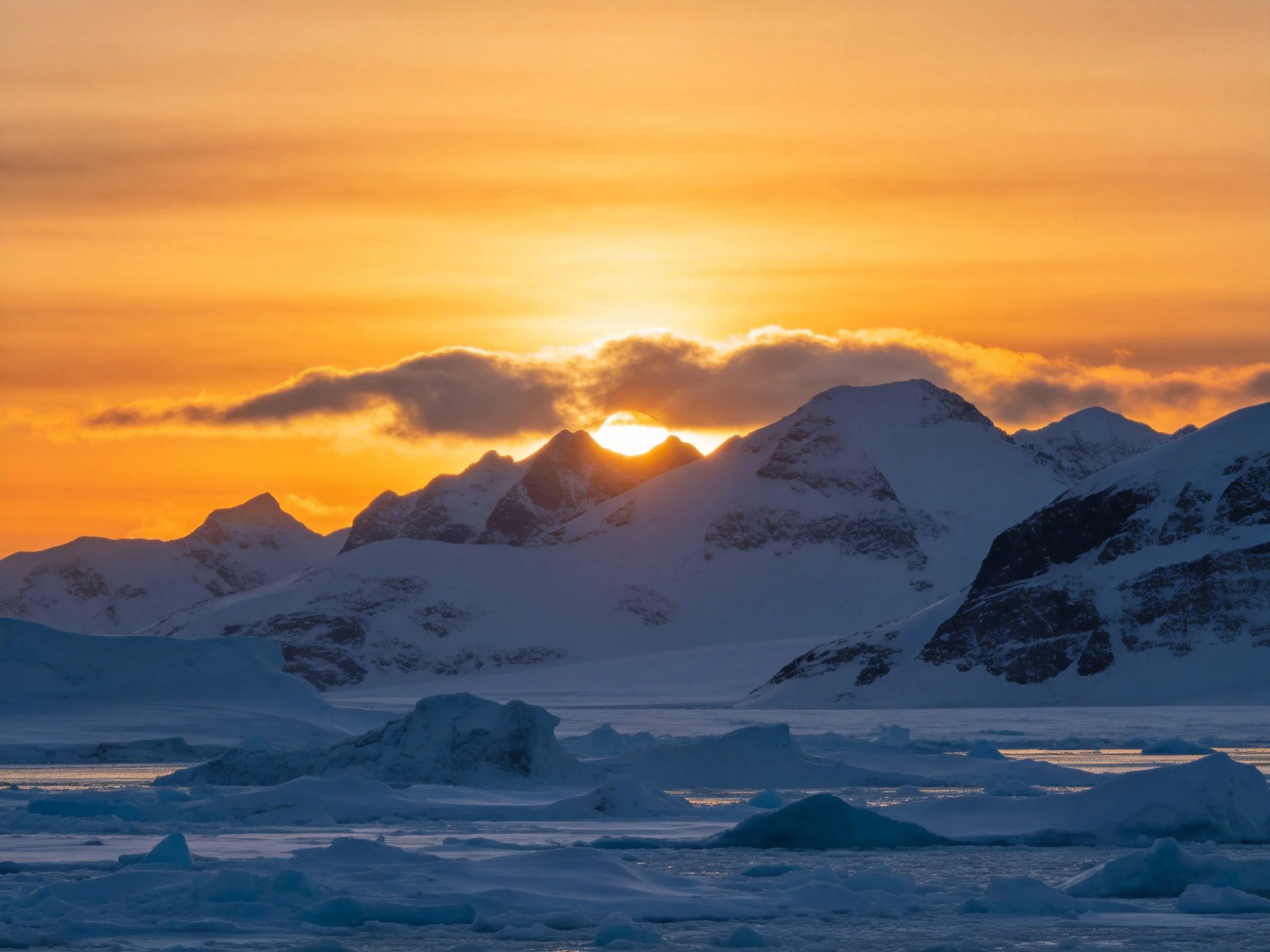 Golden sunrise illuminates snow-capped mountain peaks over icy waters