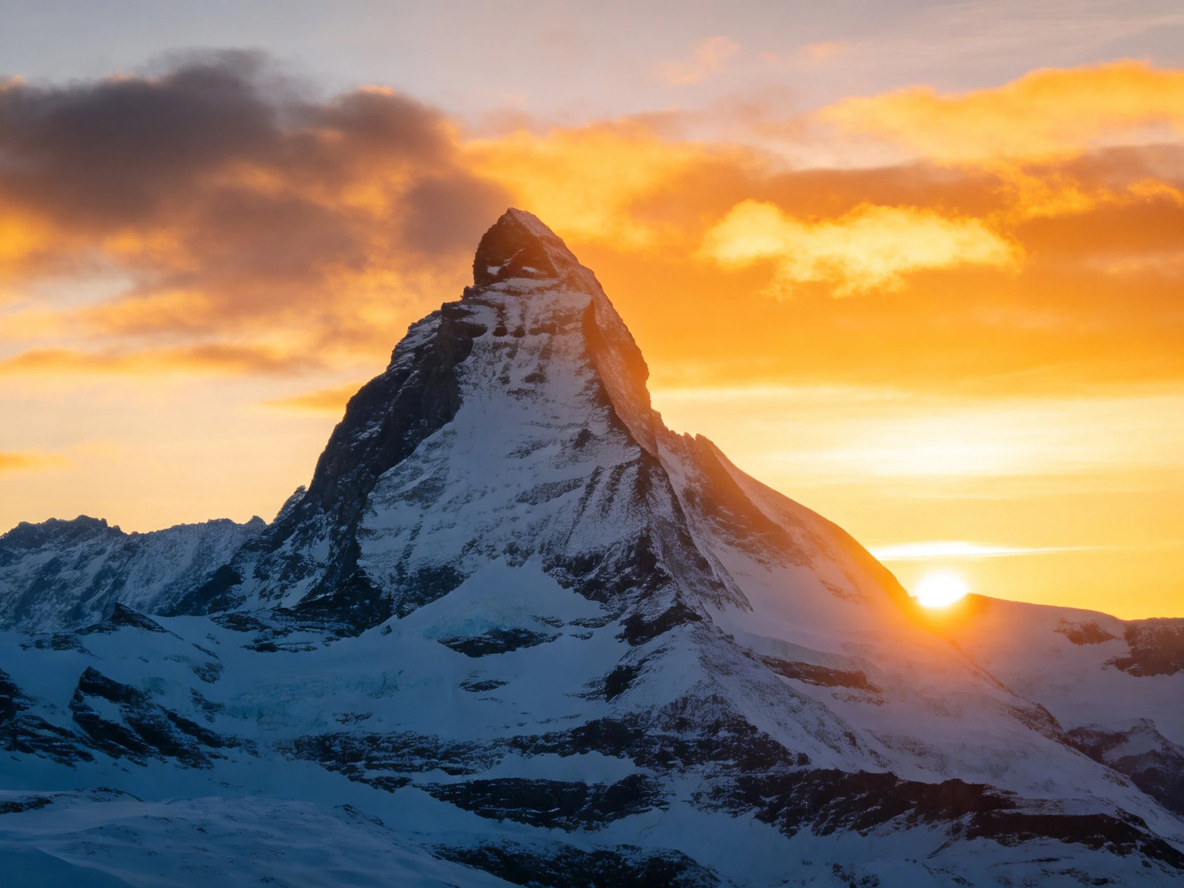 Golden sunset illuminates snow-capped mountain peak with dramatic cloud formation