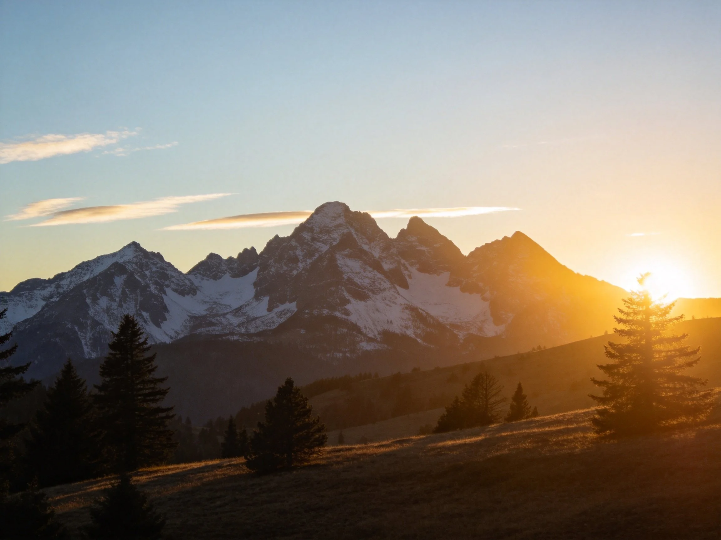 Golden sunset illuminates snow-capped mountain peaks with pine trees