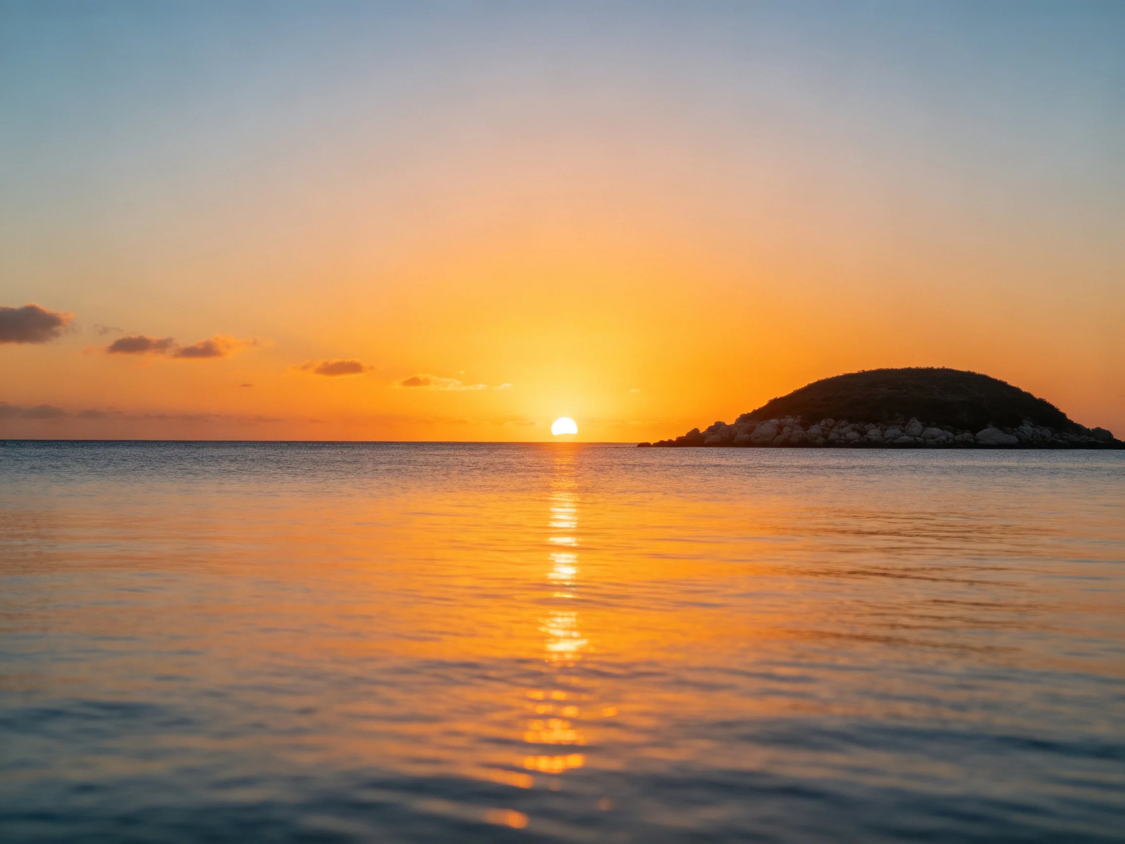 Golden sunset over calm seas next to a rocky island
