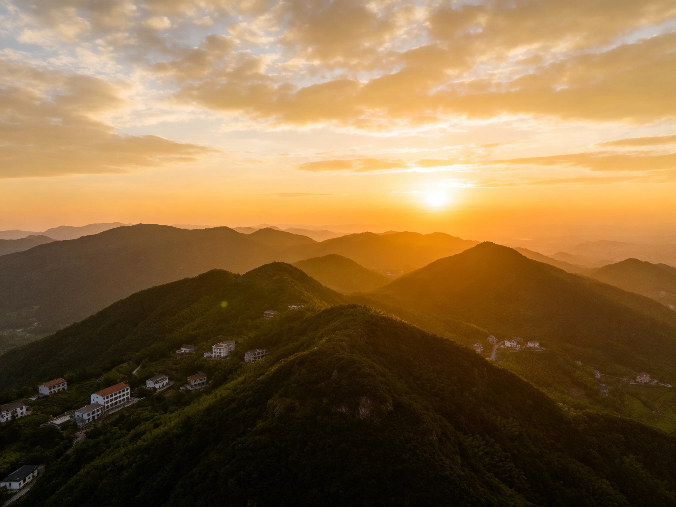 Golden sunset over rolling green mountains with scattered white homes