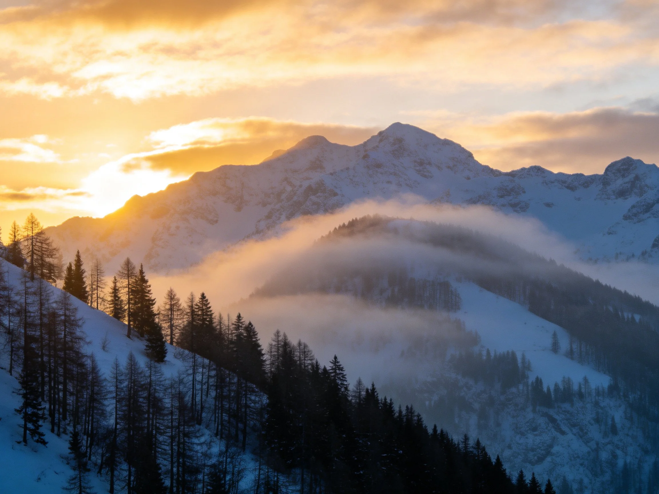 Golden sunset over snow-capped mountain peaks with misty forests
