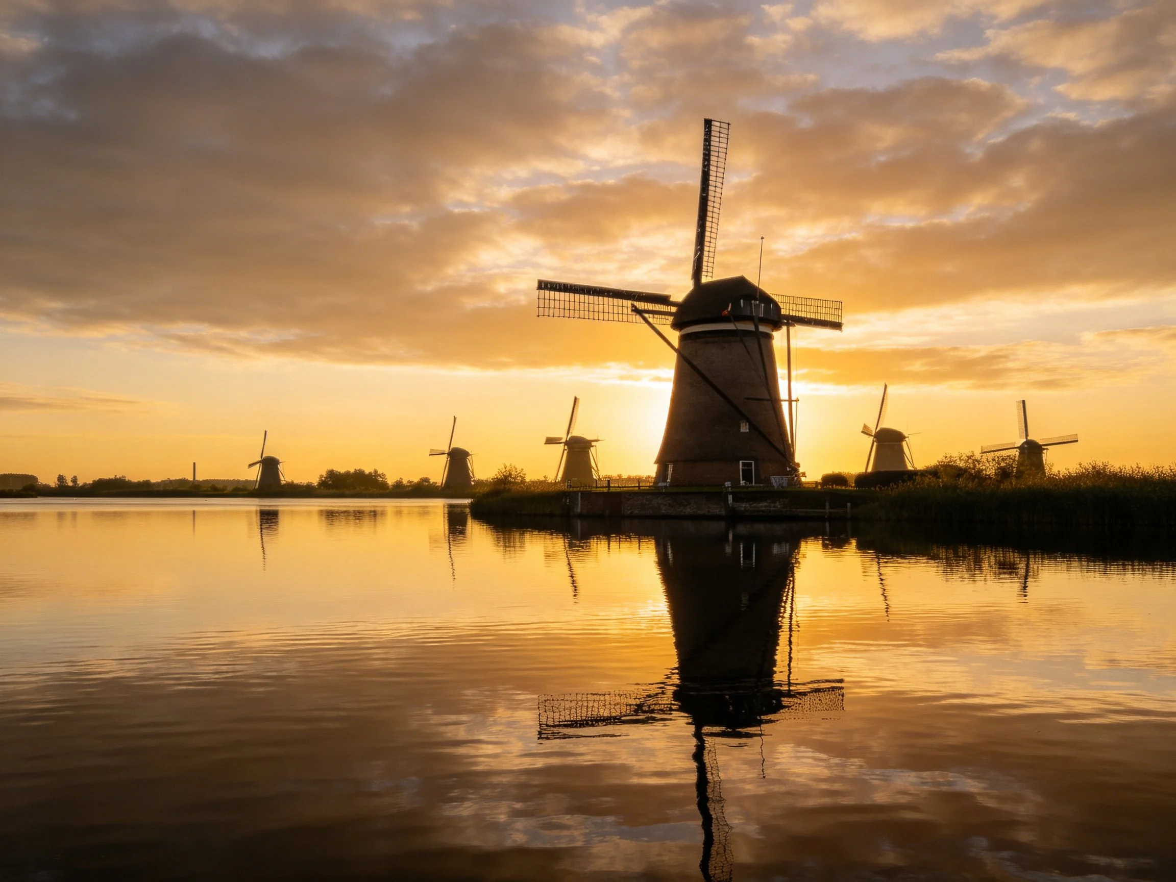 Golden sunset over traditional windmills with mirror-like reflections