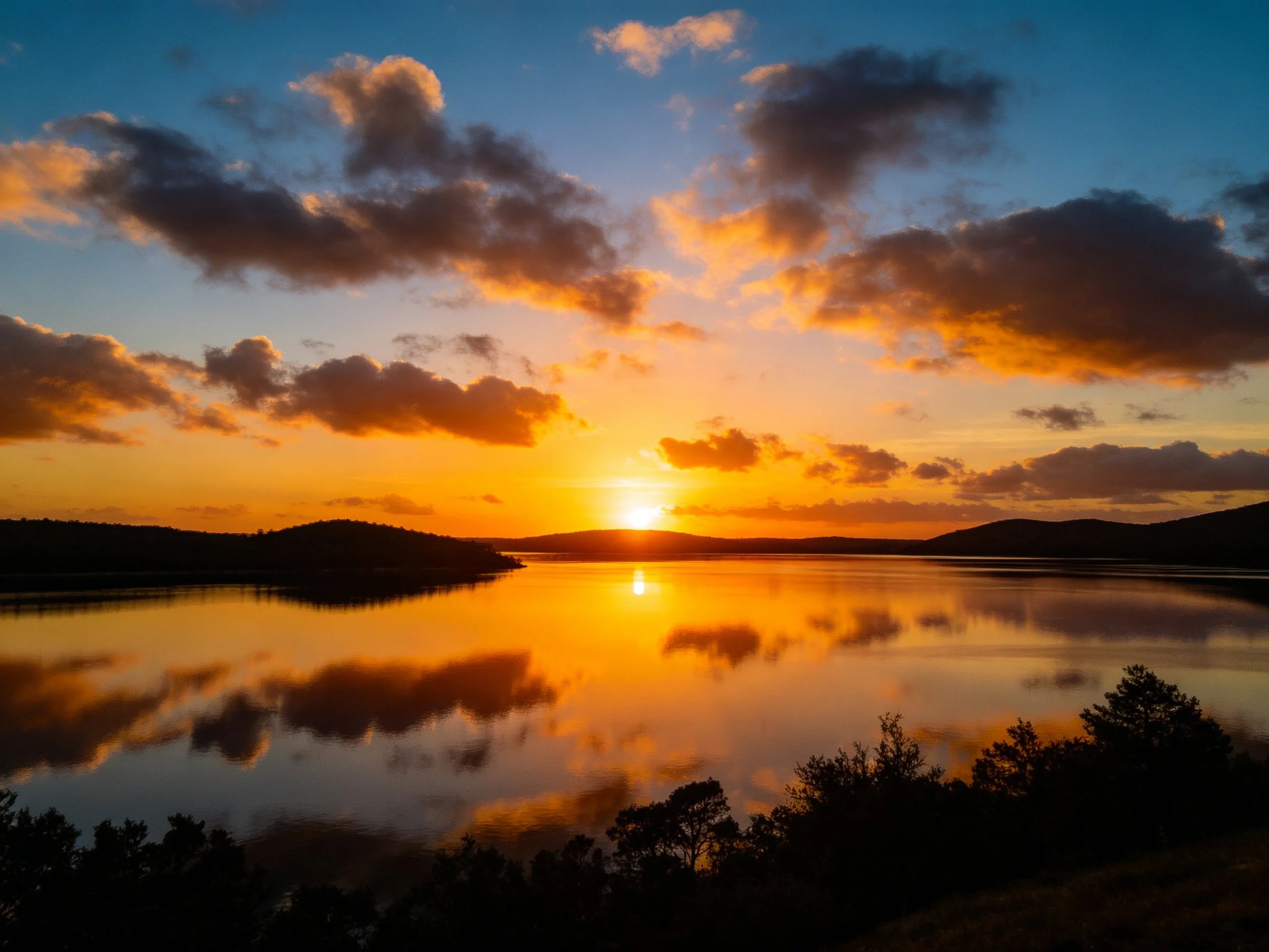 Golden sunset reflects on calm lake with dramatic clouds