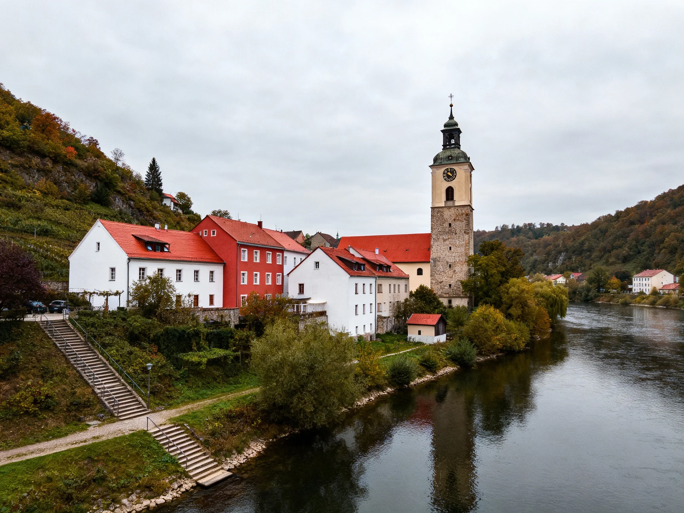 Historic buildings with red roofs by a calm river and clock tower