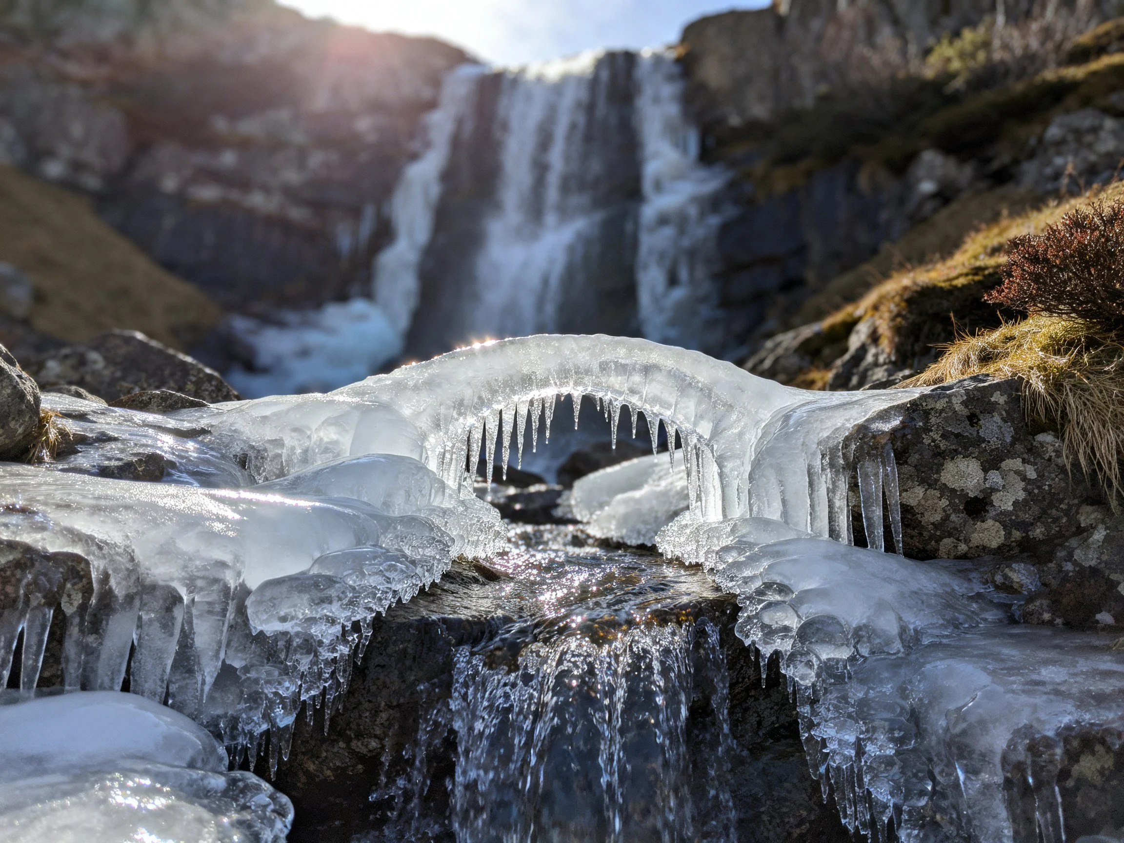 Icy arch bridging frozen stream beneath cascading waterfall