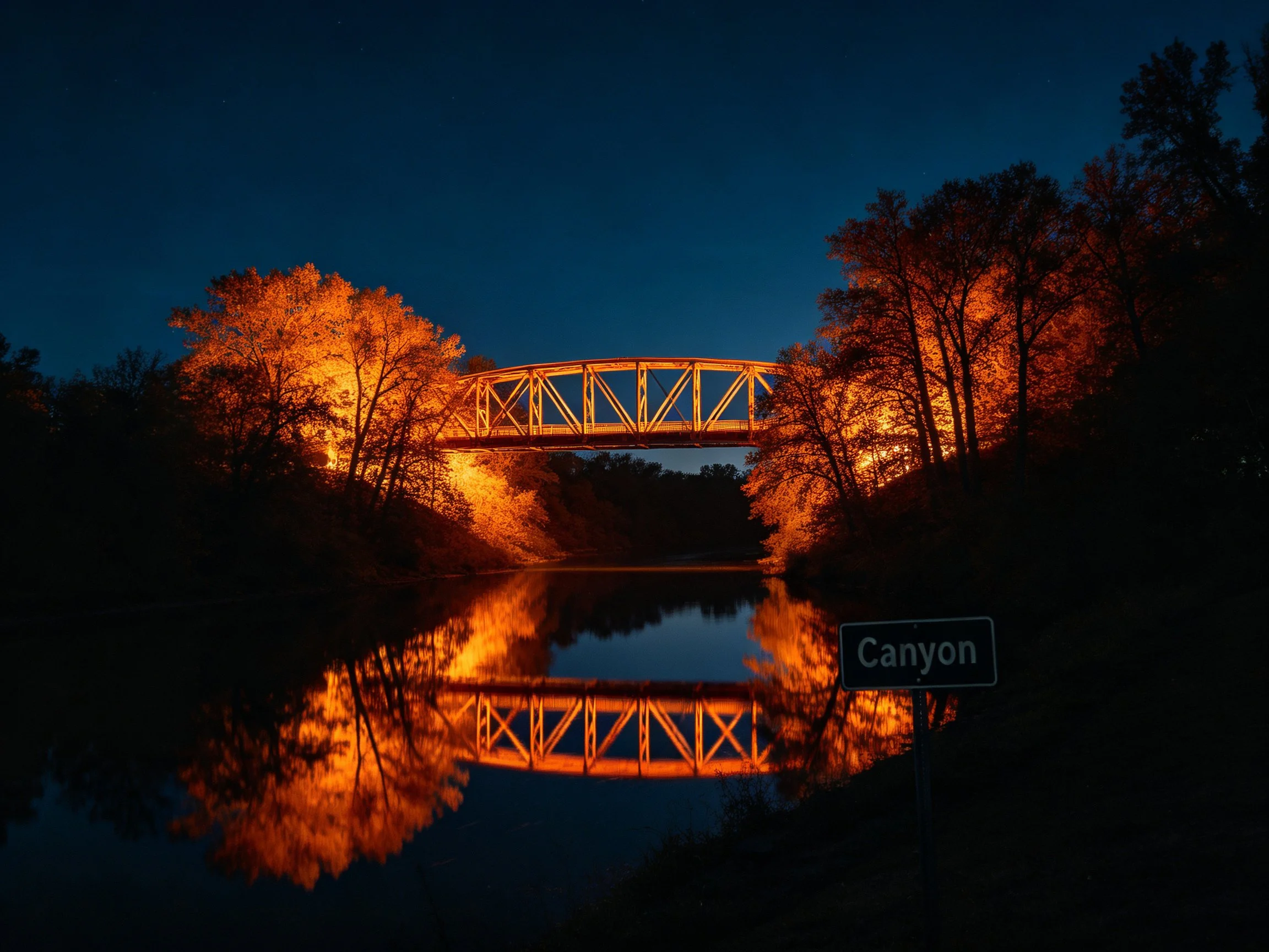 Illuminated metal bridge spans calm water at dusk