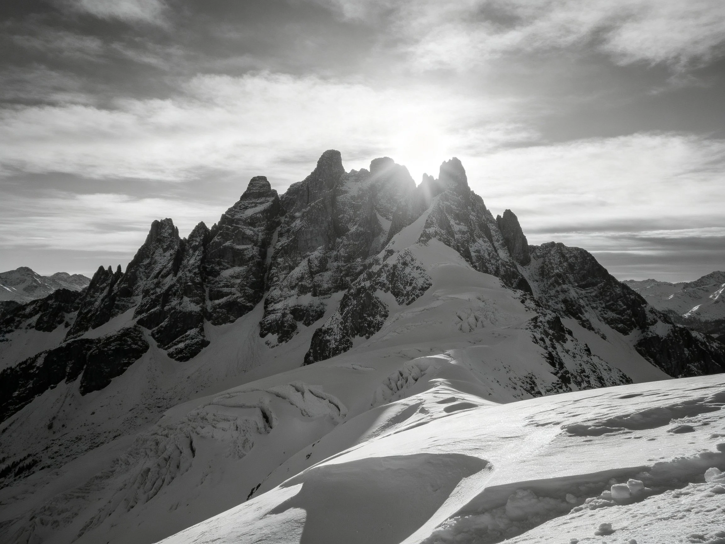 Jagged mountain peaks tower over snowy slopes under bright sunlight