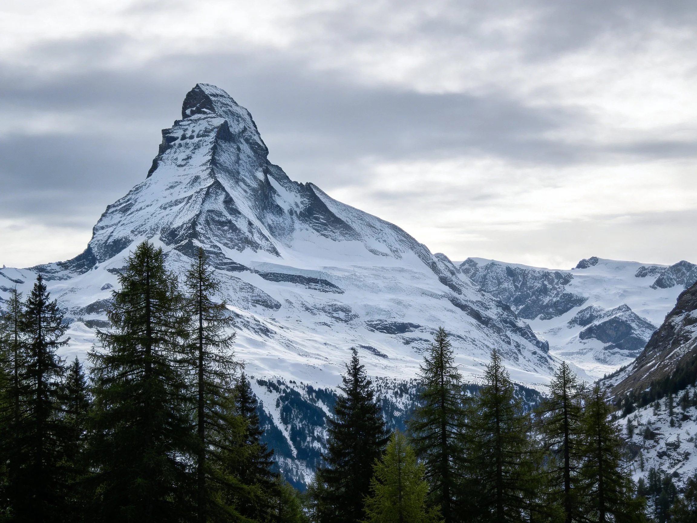 Large snow-capped triangular mountain peak with dark rocky base and forest below