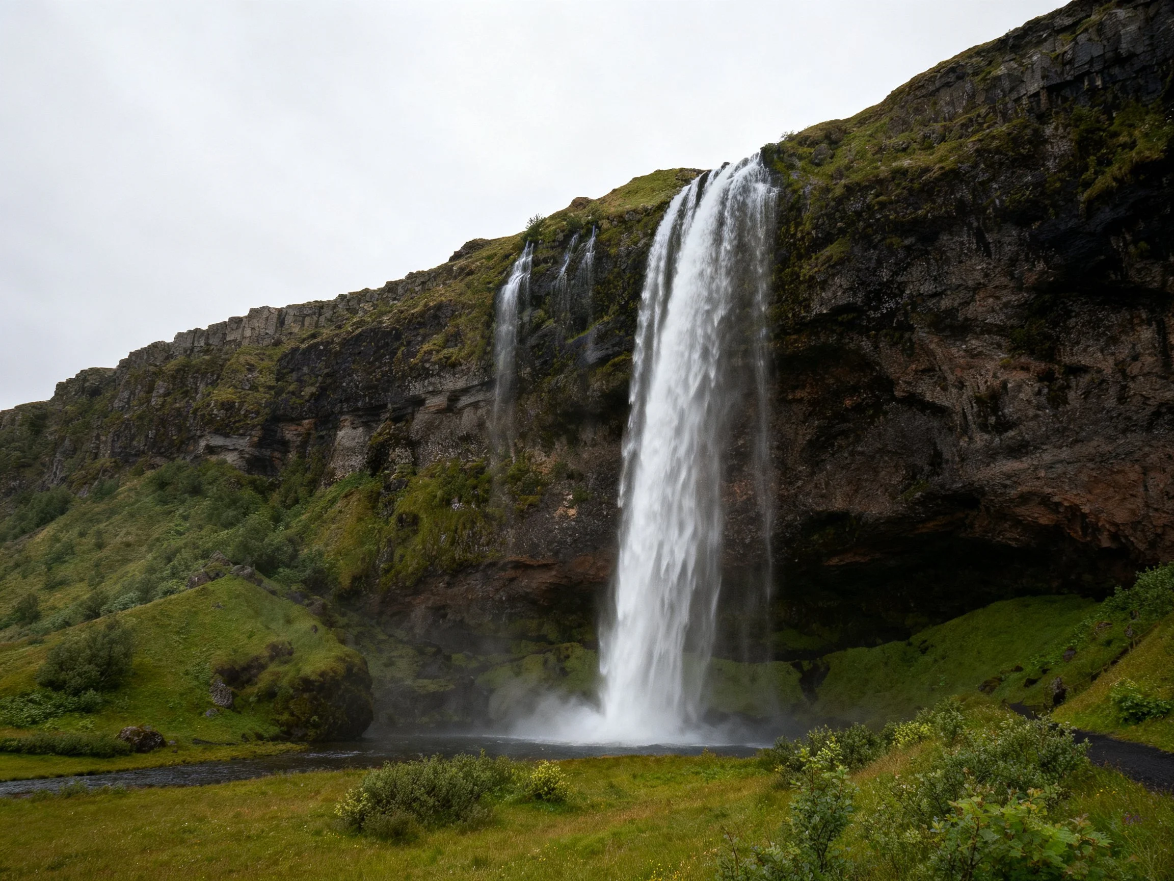 Large waterfall drops from moss-covered cliff into misty basin