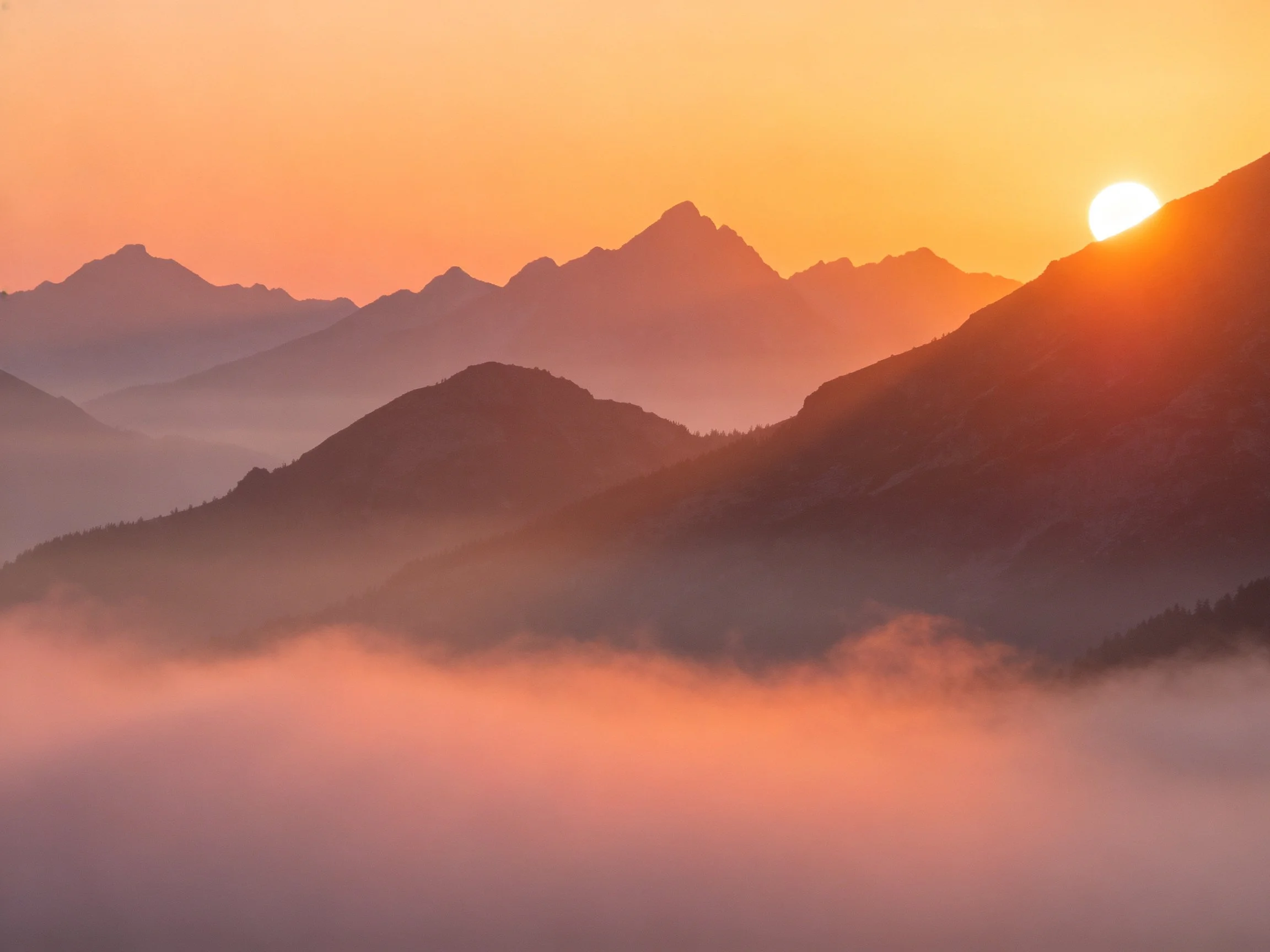 Layered Mountain Peaks at Sunrise with Mist and Warm Hues