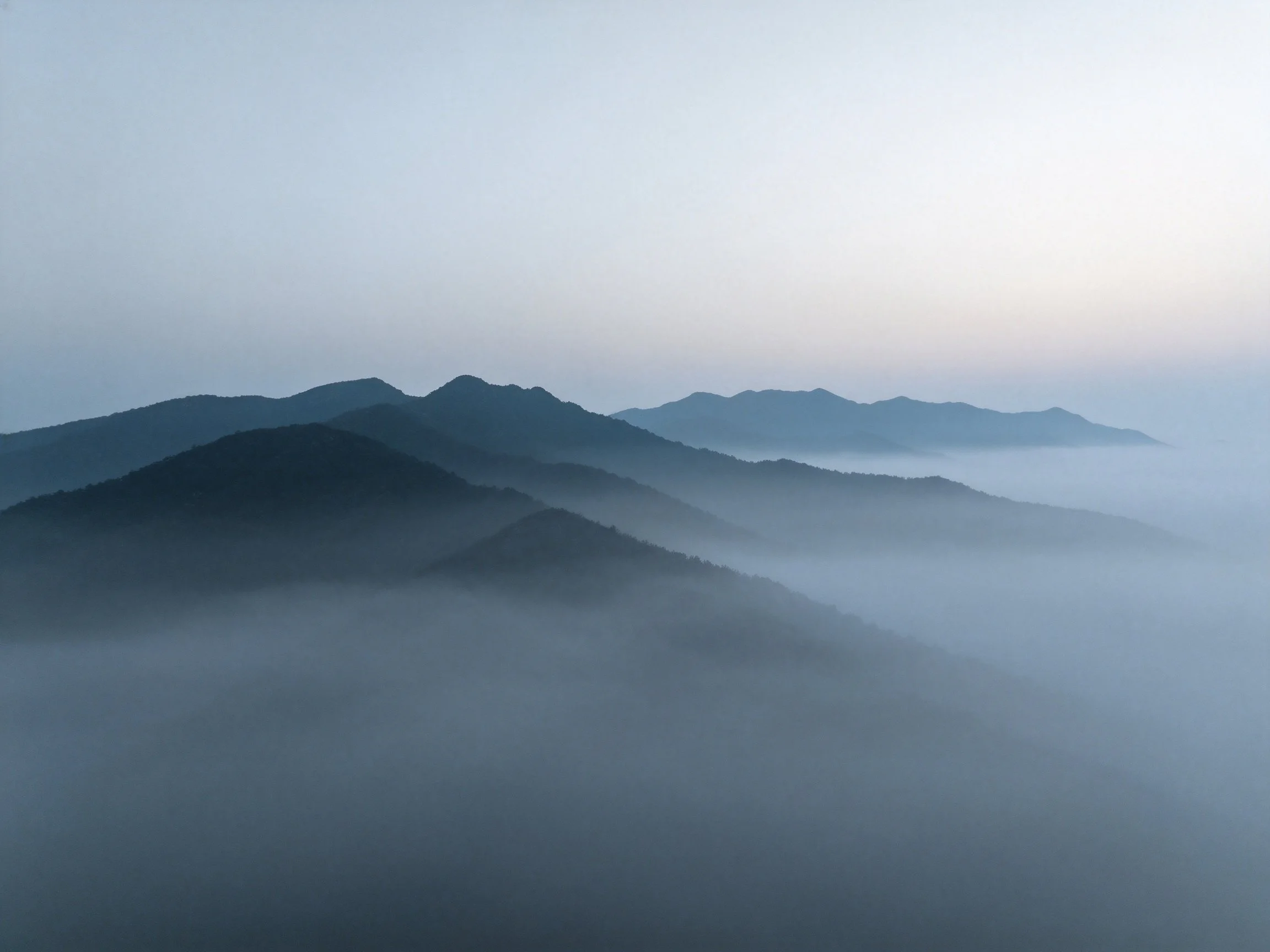 Layered mountain peaks shrouded in misty fog under soft pastel sky