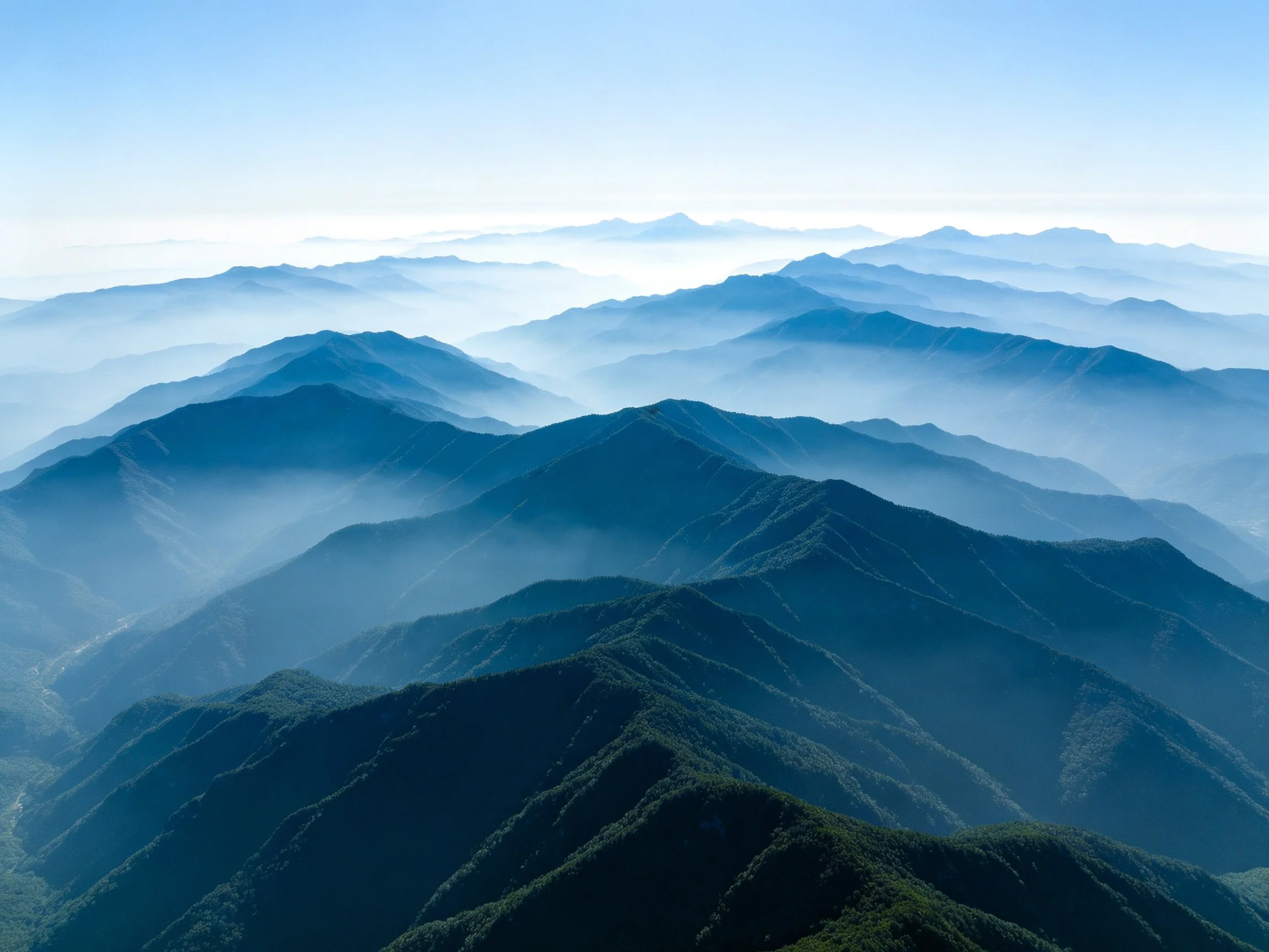 Layers of mist-covered blue-green mountains under clear sky