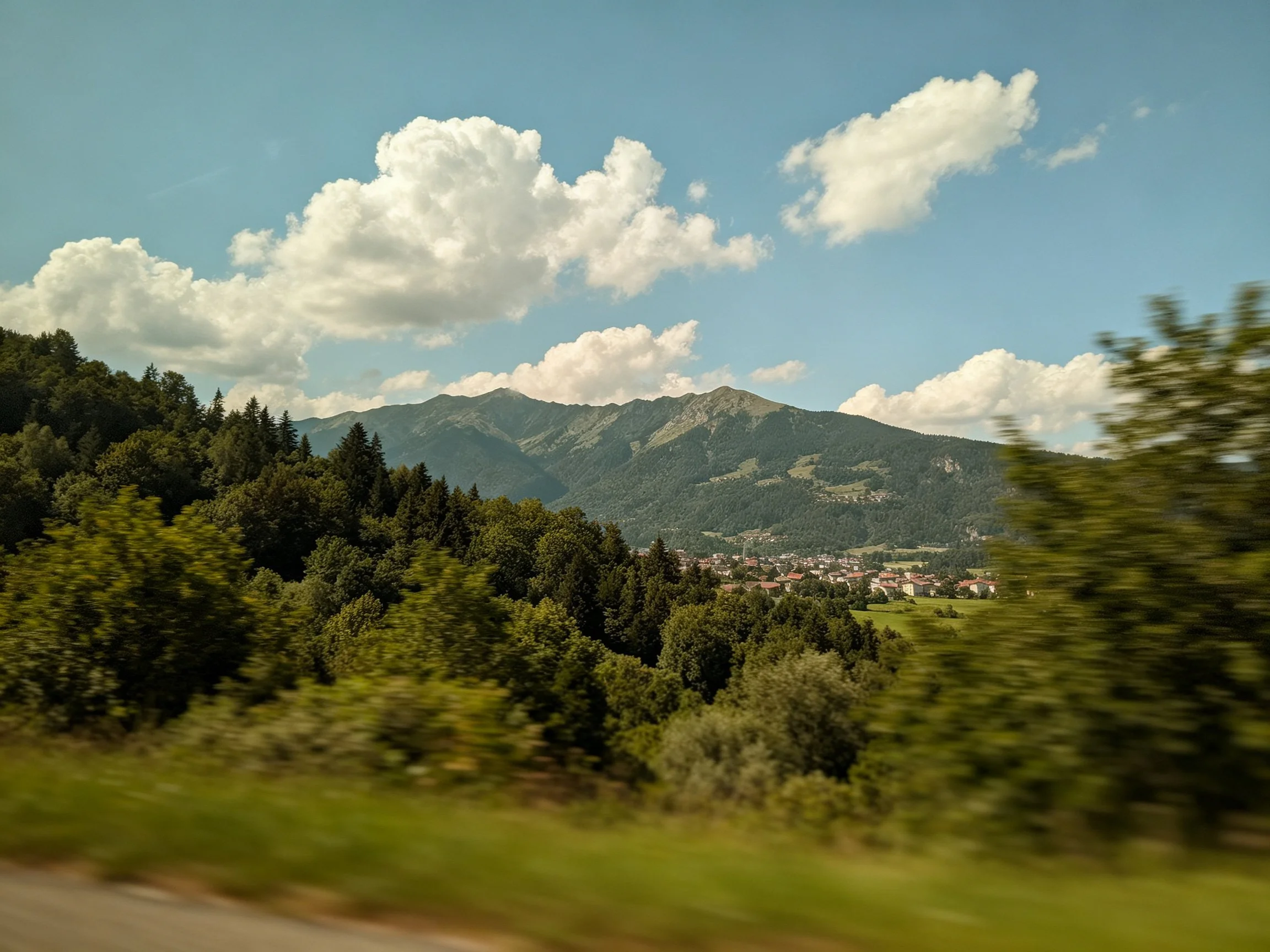 Lush green forests, rolling mountains, and a town beneath sunny sky