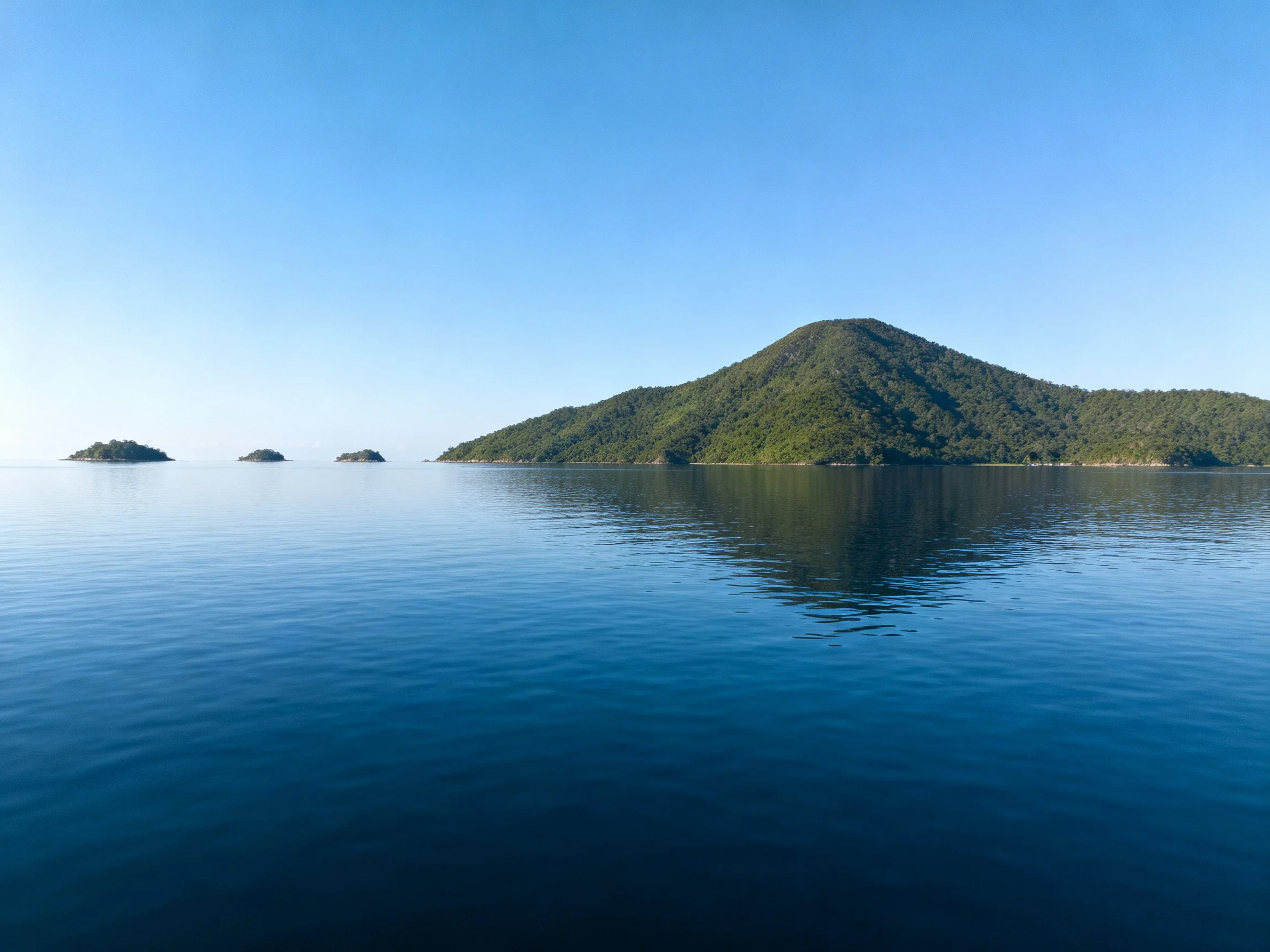 Lush green island surrounded by calm blue waters and distant islets