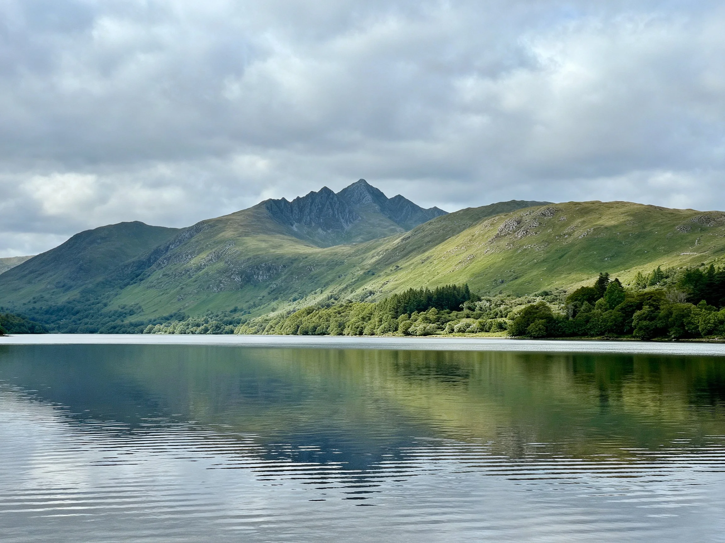 Lush green mountains reflected in calm lake under cloudy sky