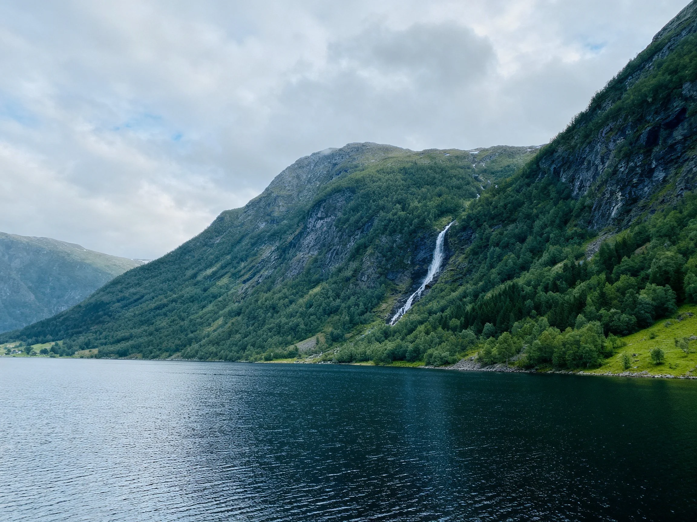 Lush green mountains with a waterfall beside deep blue calm waters