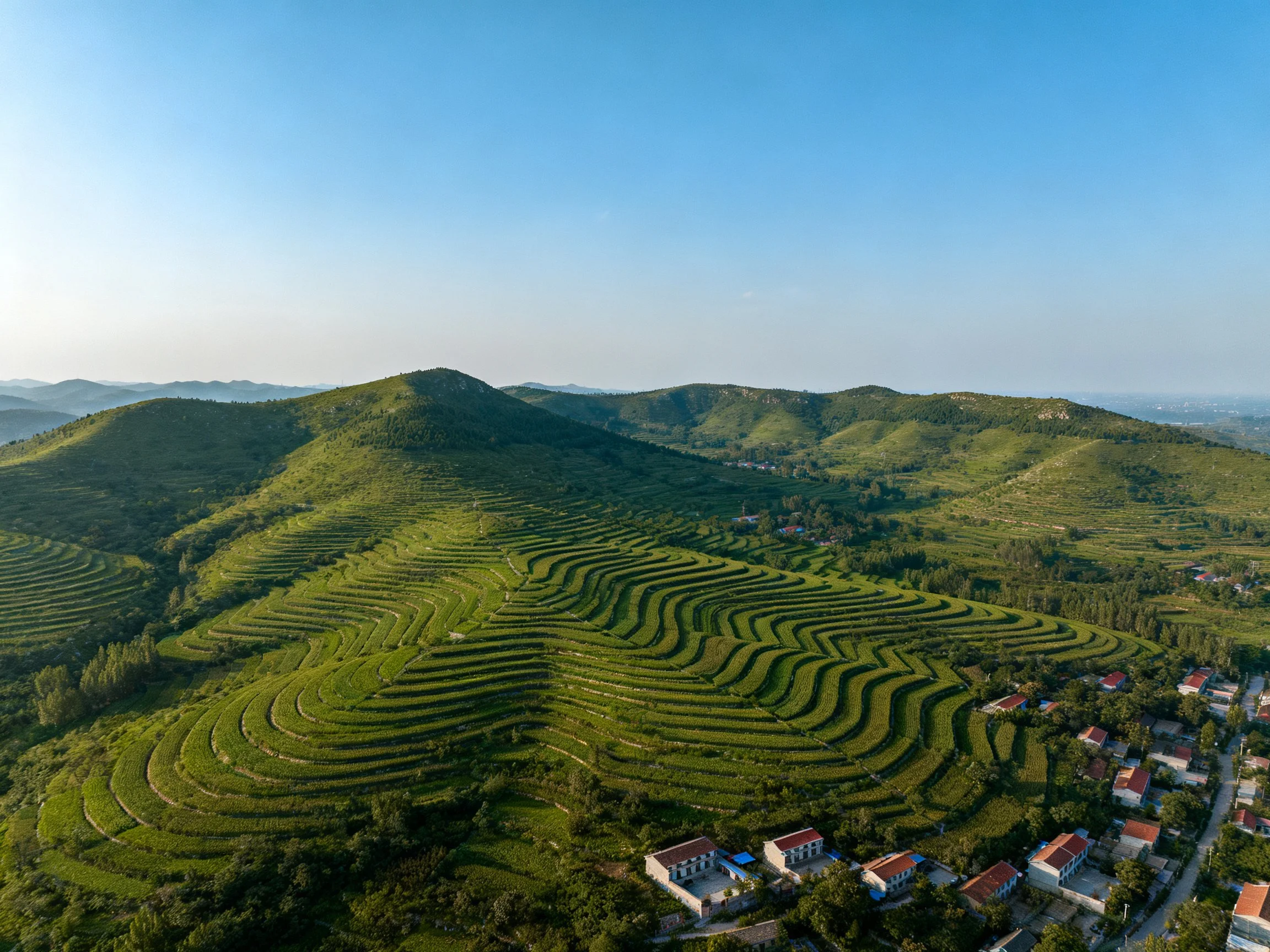 Lush green terraced hills surround a small village amid rolling mountains