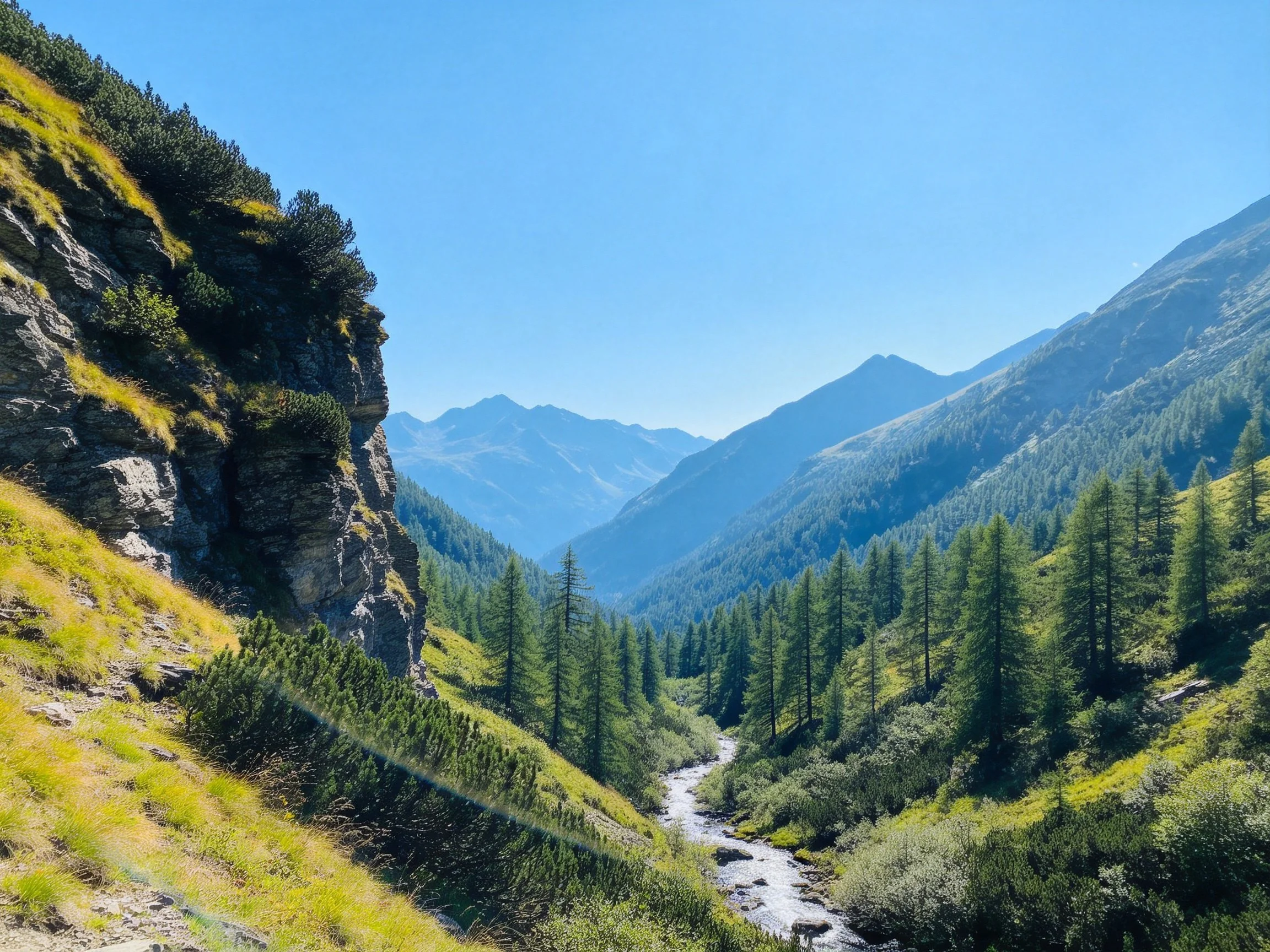 Lush green valley with rocky cliffs, winding stream, and distant mountains