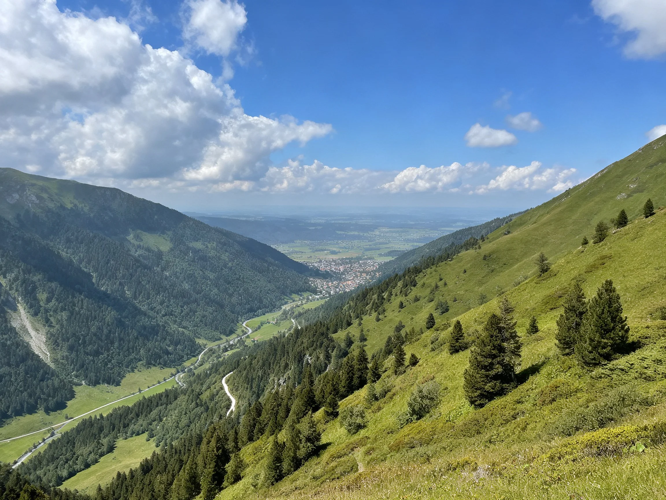 Lush mountain valley with green slopes, distant town, and bright blue sky